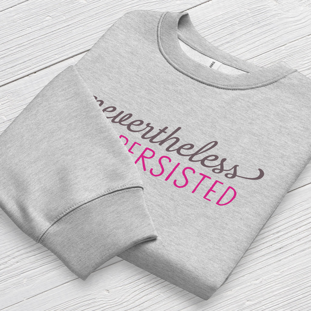 Athletic heather sweatshirt with styled text that reads "nevertheless, she persisted", folded flat showing graphic and cuff detail.