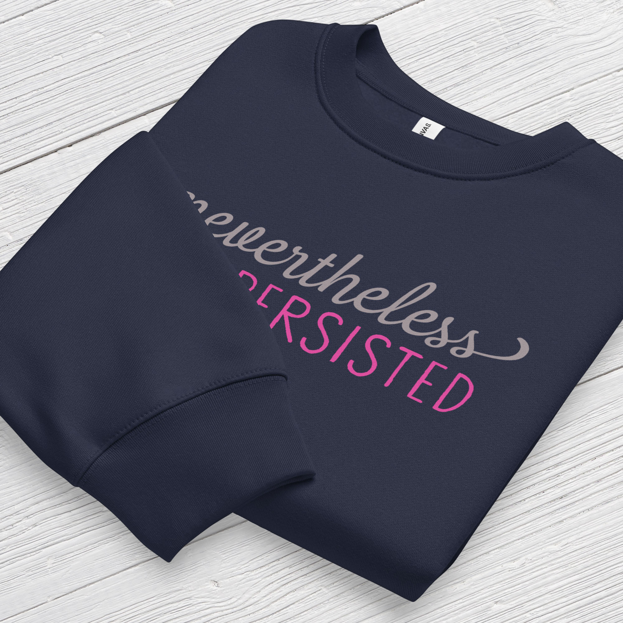 Navy sweatshirt with styled text that reads "nevertheless, she persisted", folded flat showing graphic and cuff detail.