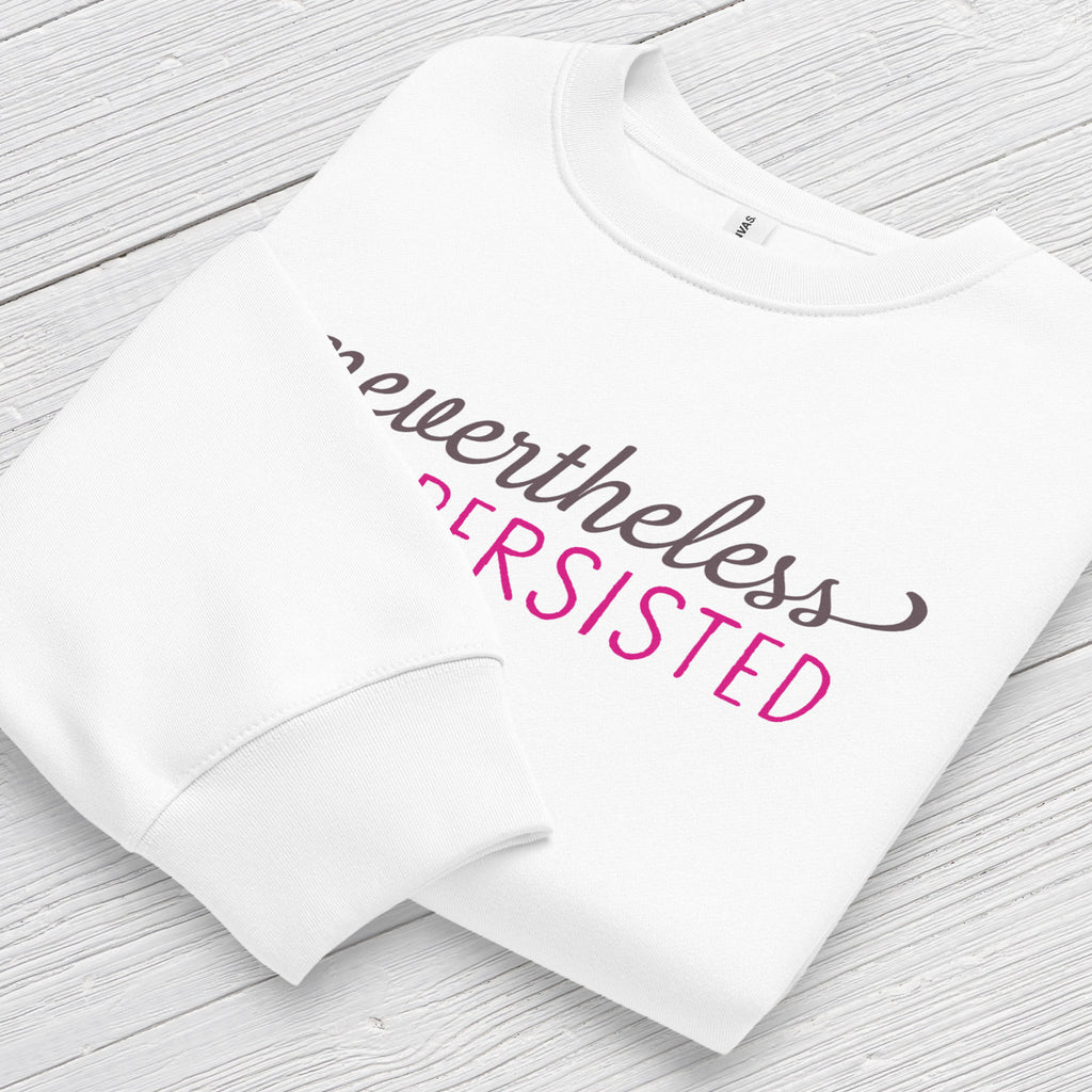 White sweatshirt with styled text that reads "nevertheless, she persisted", folded flat showing graphic and cuff detail.
