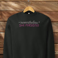 Black sweatshirt with styled text that reads "nevertheless, she persisted", hanging on a hanger.