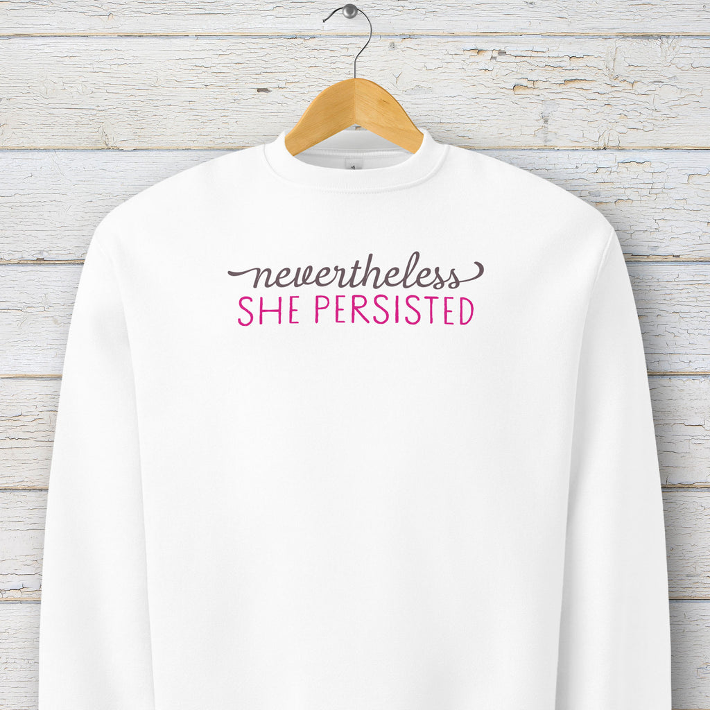 White sweatshirt with styled text that reads "nevertheless, she persisted", hanging on a hanger.