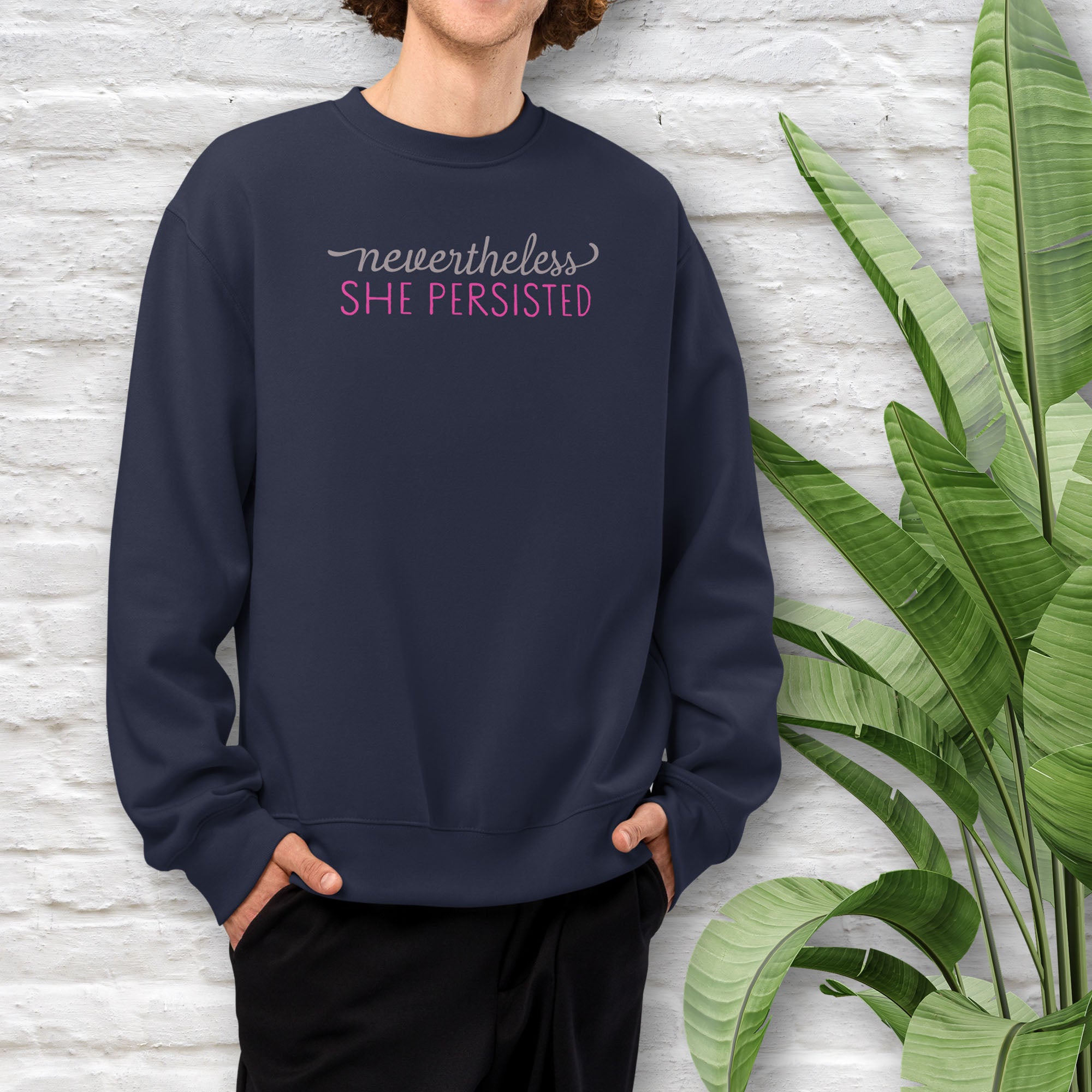 Navy model wearing black sweatshirt with styled text that reads "nevertheless, she persisted".