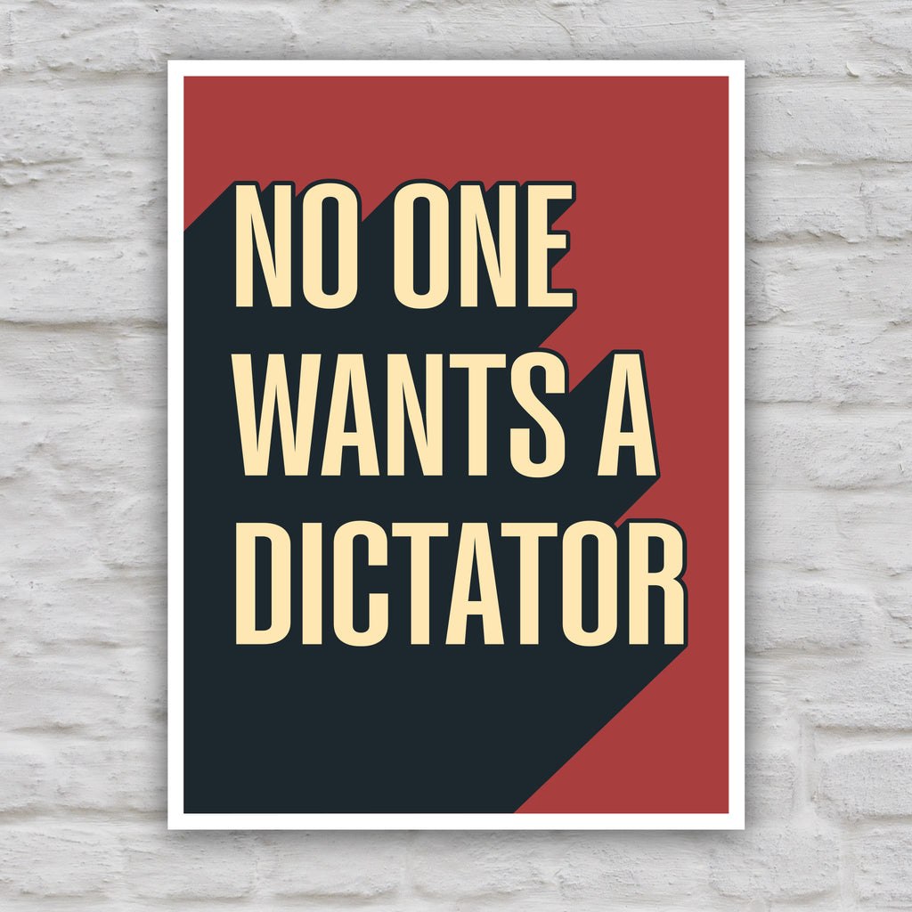 Color version of anti-Trump protest sign with bold text reading “No One Wants a Dictator” in cream letters on red background with black shadow.