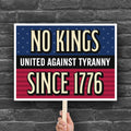 Bold protest sign with blue and red stars and stripes background and gold and white text reading "No Kings – United Against Tyranny – Since 1776" – a defiant, anti-Trump message rejecting authoritarianism and honoring America's revolutionary roots.
