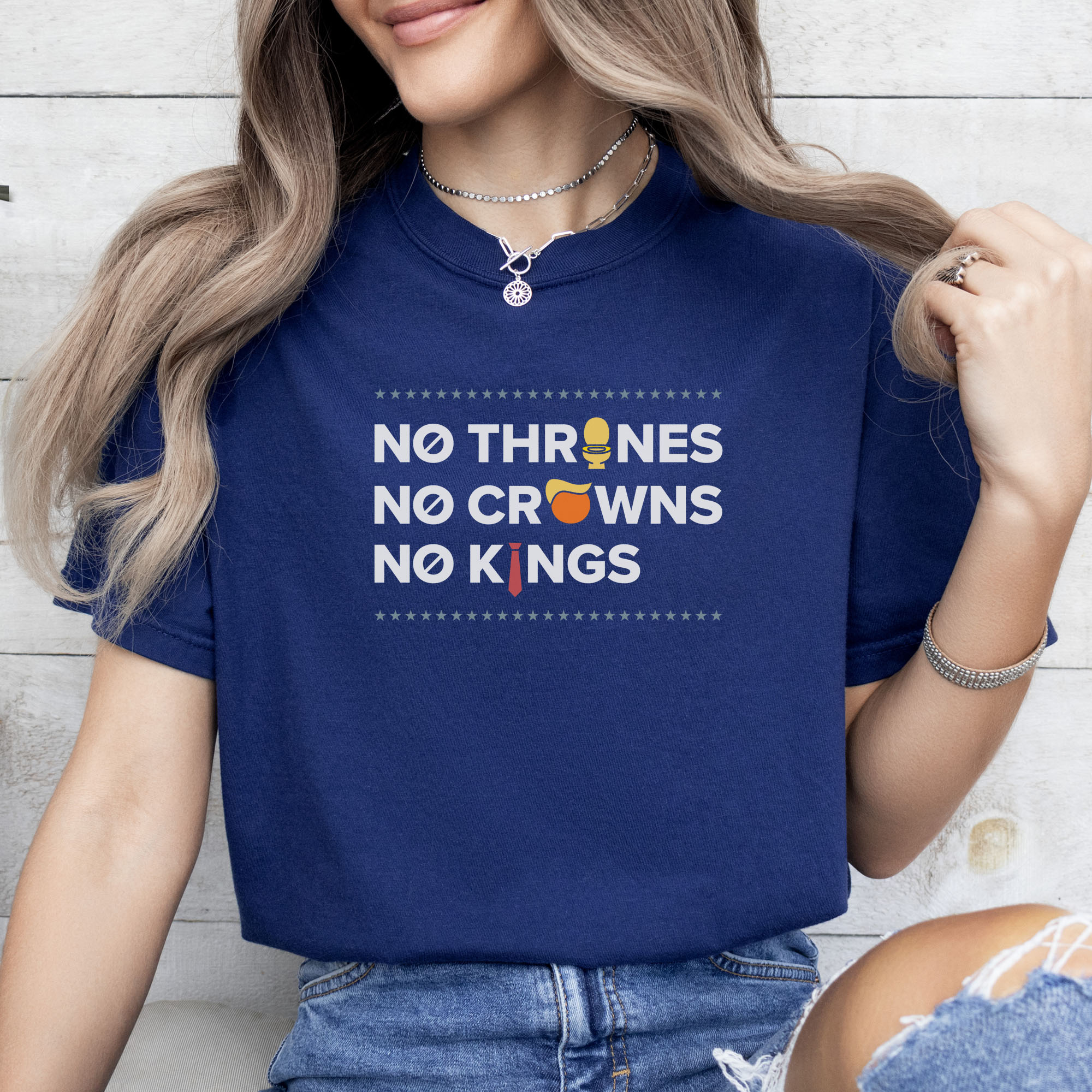 Female model wearing true navy t-shirt with bold text reading “No Thrones No Crowns No Kings” featuring satirical Trump graphics: gold toilet, yellow hair, and long red tie, original anti-Trump protest shirt.