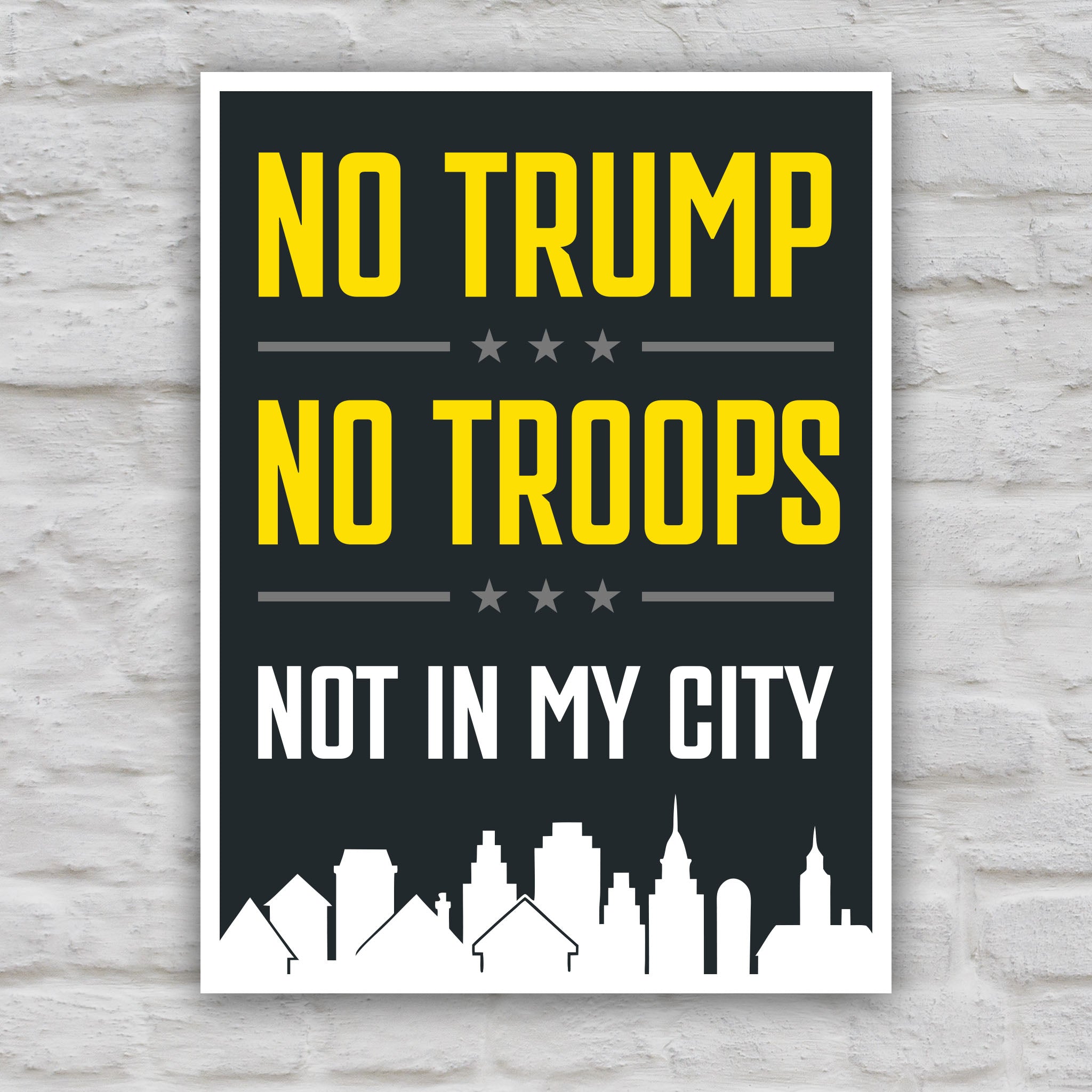 Color version of protest sign with bold yellow and white text reading “No Trump No Troops Not in My City” over a dark background with a city skyline silhouette.