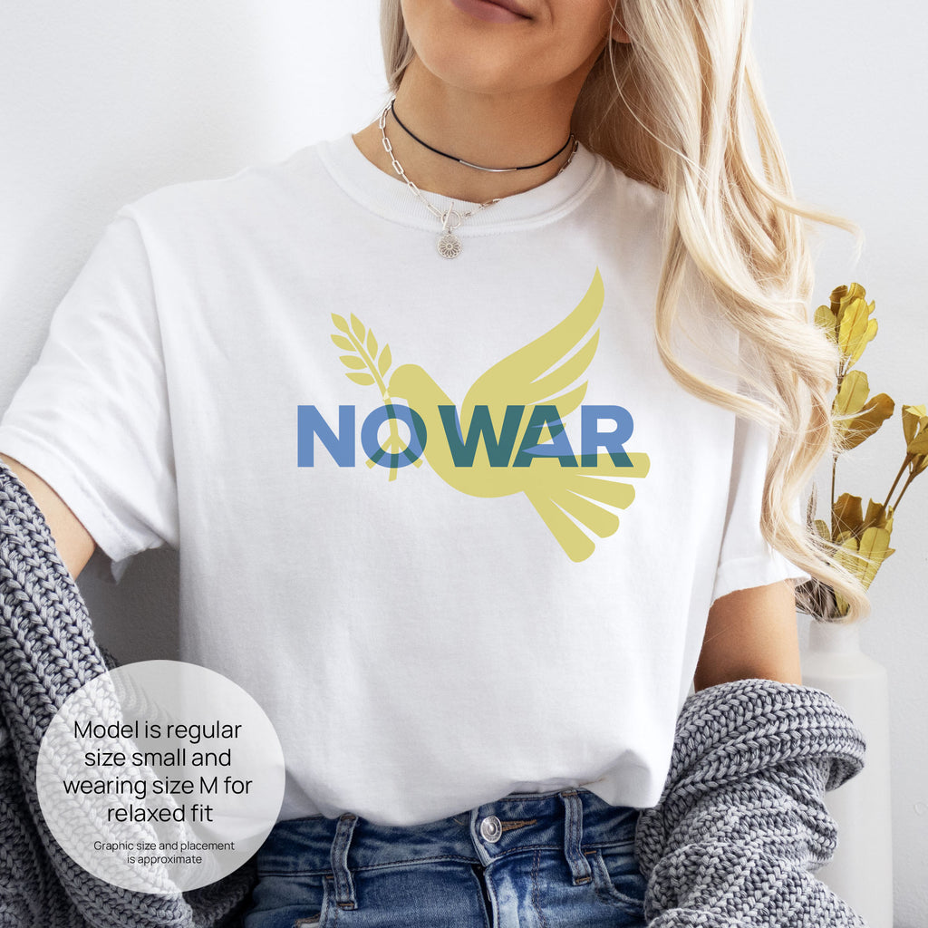 Female model wearing white t-shirt featuring blue “No War” text over a yellow peace dove carrying an olive branch that forks into a peace sign over the text. Includes size and fit information for the model who is regular size small, and wearing a size M shirt for a relaxed fit.
