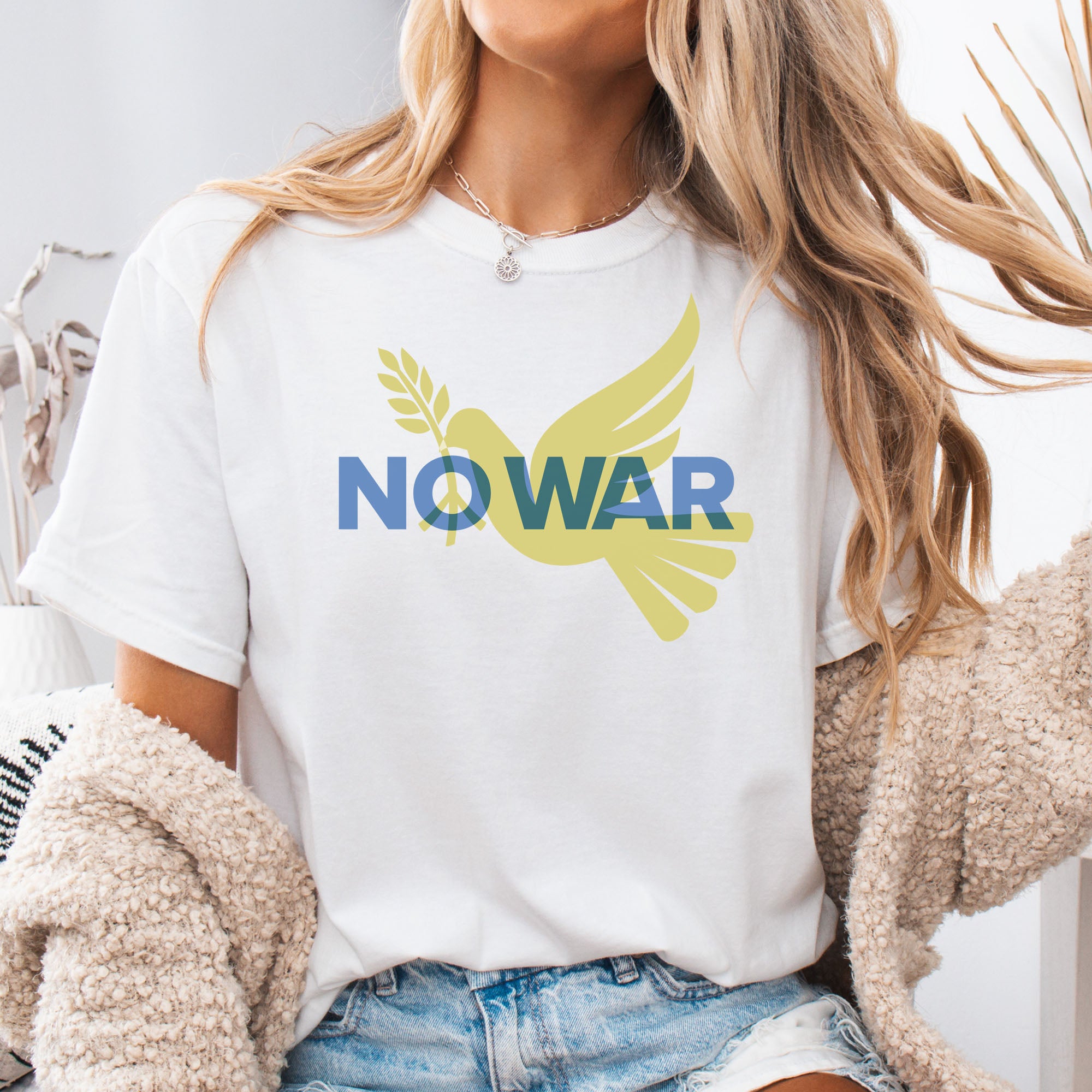 Female model wearing white t-shirt featuring blue “No War” text over a yellow peace dove carrying an olive branch that forks into a peace sign over the text..