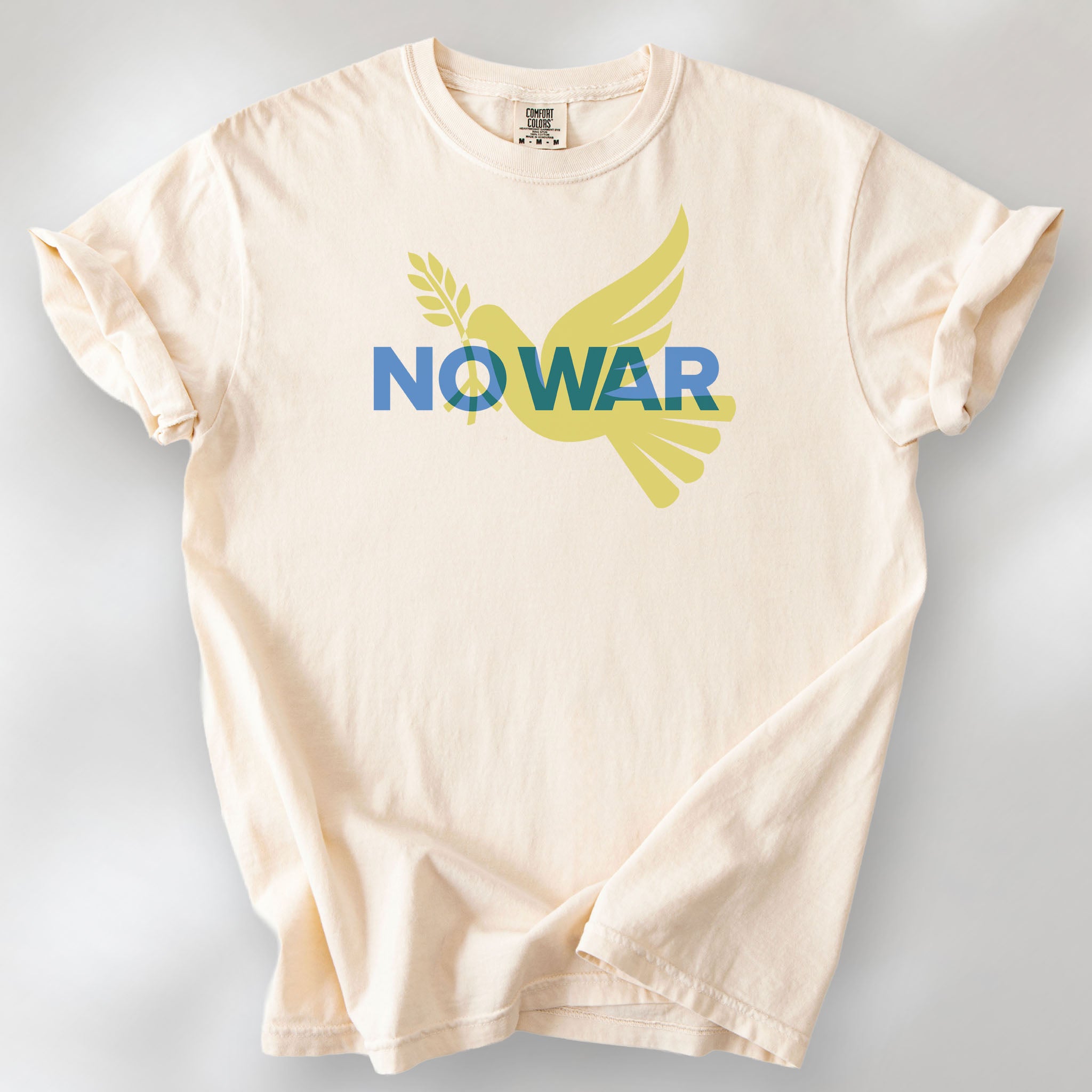 Ivory t-shirt featuring blue “No War” text over a yellow peace dove carrying an olive branch that forks into a peace sign over the text.