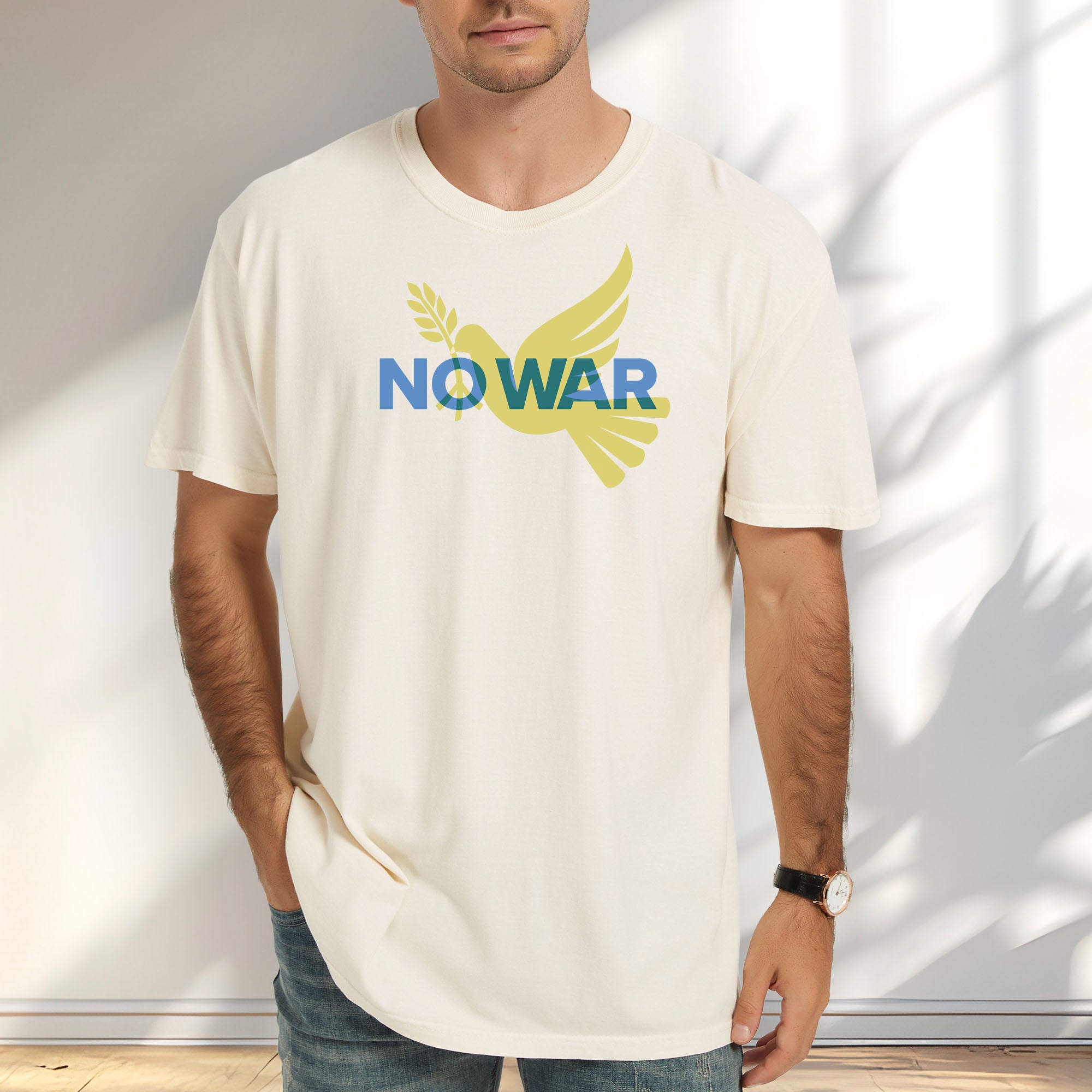 Male model wearing ivory t-shirt featuring blue “No War” text over a yellow peace dove carrying an olive branch that forks into a peace sign over the text..