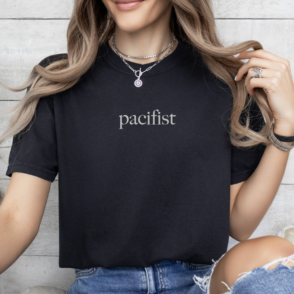 Female model wearing black t-shirt with minimalist serif text reading "pacifist."