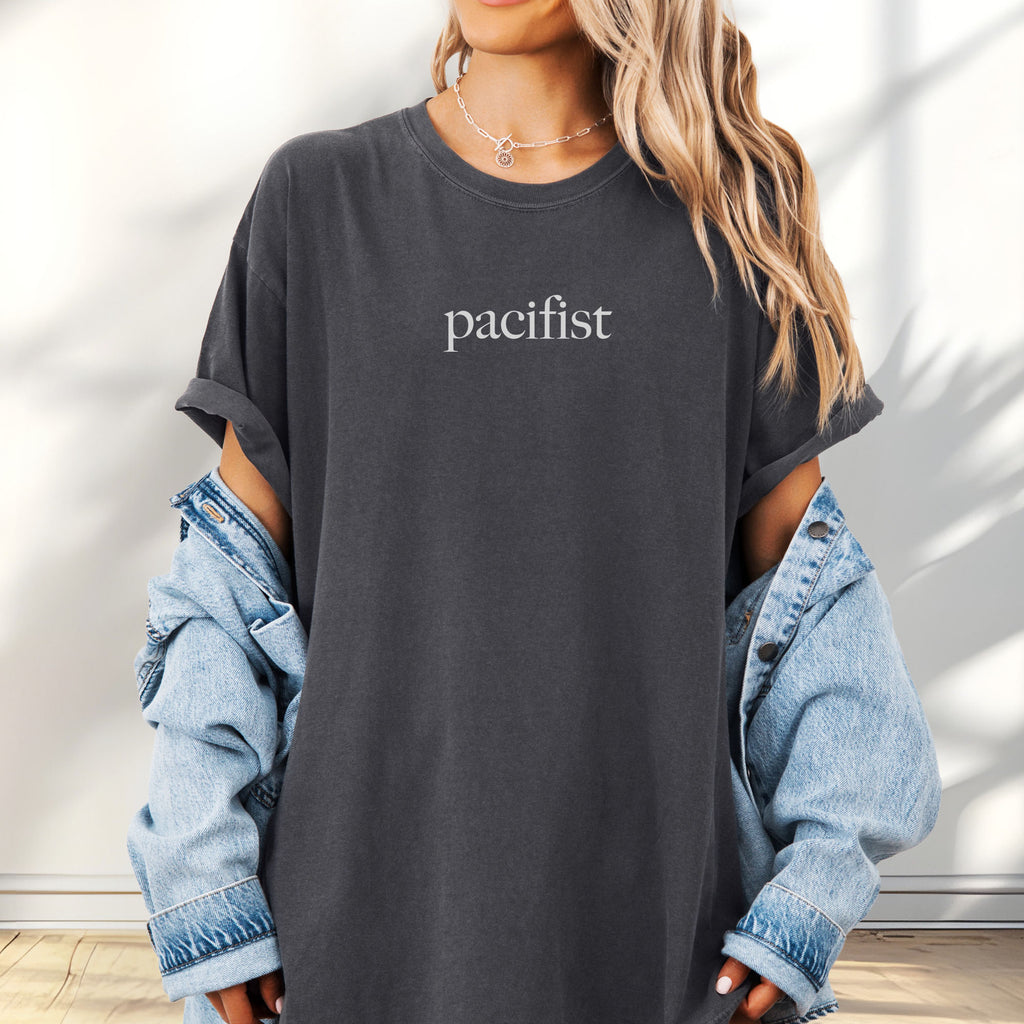 Female model wearing oversized pepper t-shirt with minimalist serif text reading "pacifist."