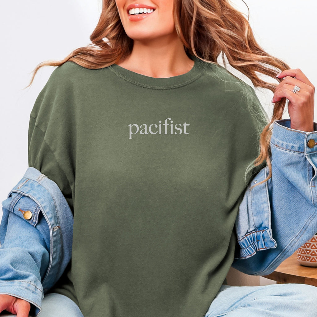 Female model wearing sage t-shirt with minimalist serif text reading "pacifist."
