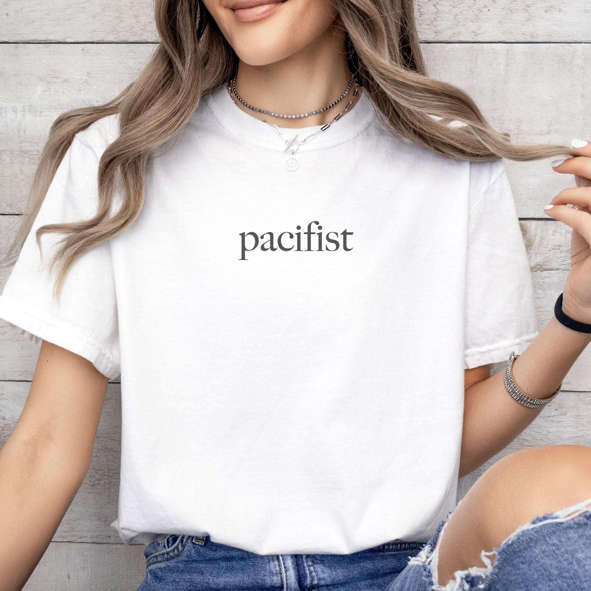 Female model wearing white t-shirt with minimalist serif text reading "pacifist."