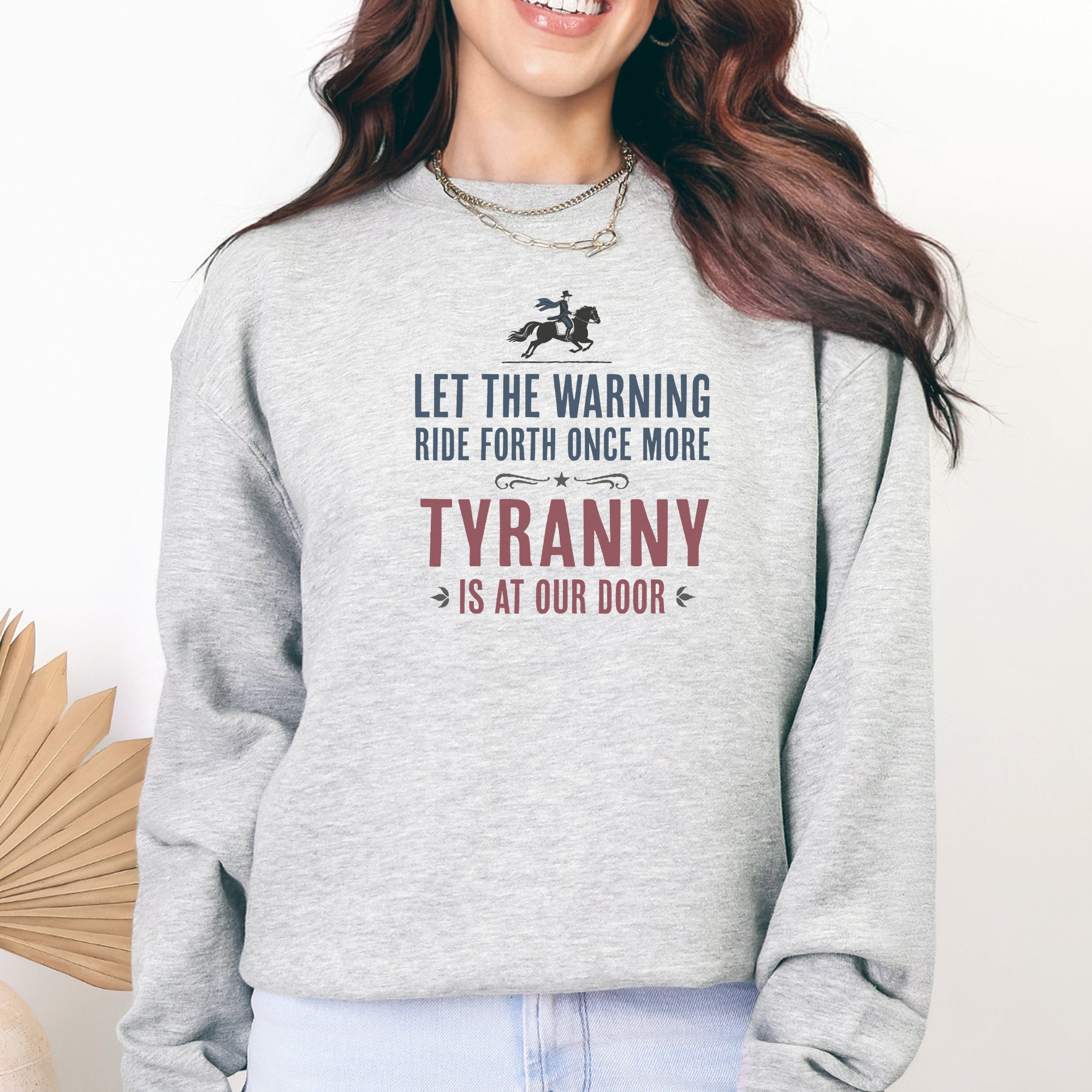 Female model wearing grey sweatshirt with a silhouette of Paul Revere on horseback and the text “Let the warning ride forth once more – Tyranny is at our door” in blue and red.