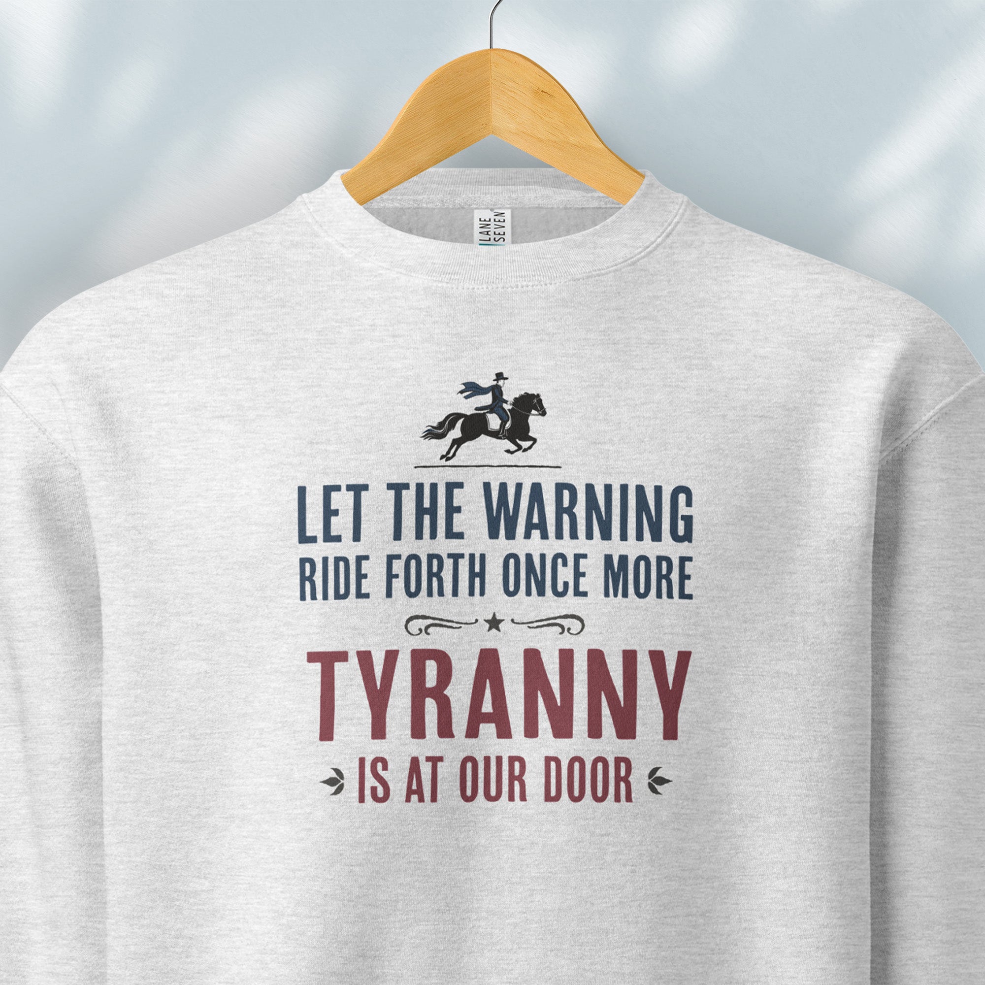 Hanging grey sweatshirt with a silhouette of Paul Revere on horseback and the text “Let the warning ride forth once more – Tyranny is at our door” in blue and red.