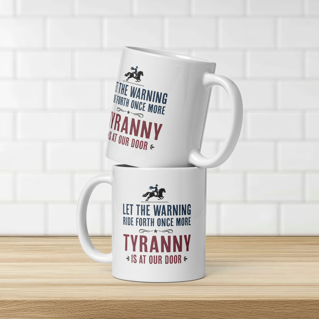 Two white ceramic coffee mugs with a historical-style design reading “Let the warning ride forth once more — Tyranny is at our door,” stacked on a kitchen counter showing design on both sides.