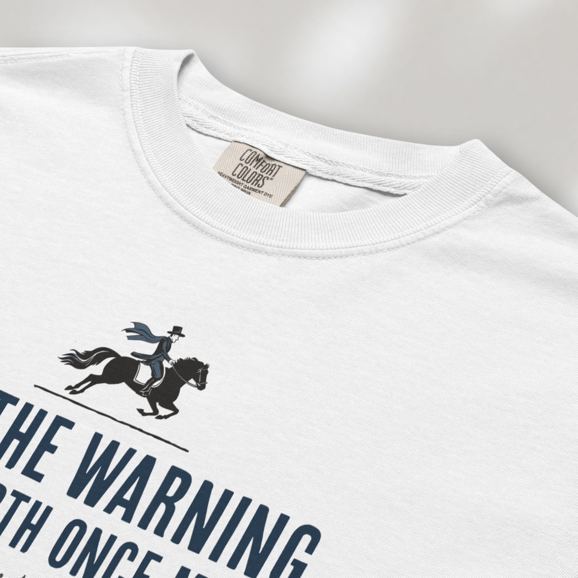 Closeup detail of white t-shirt with a silhouette of Paul Revere on horseback and the text “Let the warning ride forth once more – Tyranny is at our door” in blue and red.