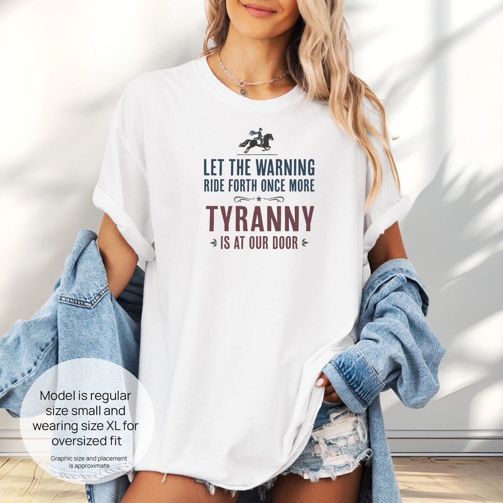 Female model wearing oversized white t-shirt with a silhouette of Paul Revere on horseback and the text “Let the warning ride forth once more – Tyranny is at our door” in blue and red. Includes size and fit information for the model who is regular size small, and wearing a size XL shirt for an oversized fit.
