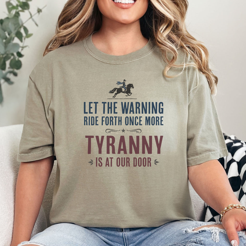 Female model wearing khaki t-shirt with a silhouette of Paul Revere on horseback and the text “Let the warning ride forth once more – Tyranny is at our door” in blue and red.