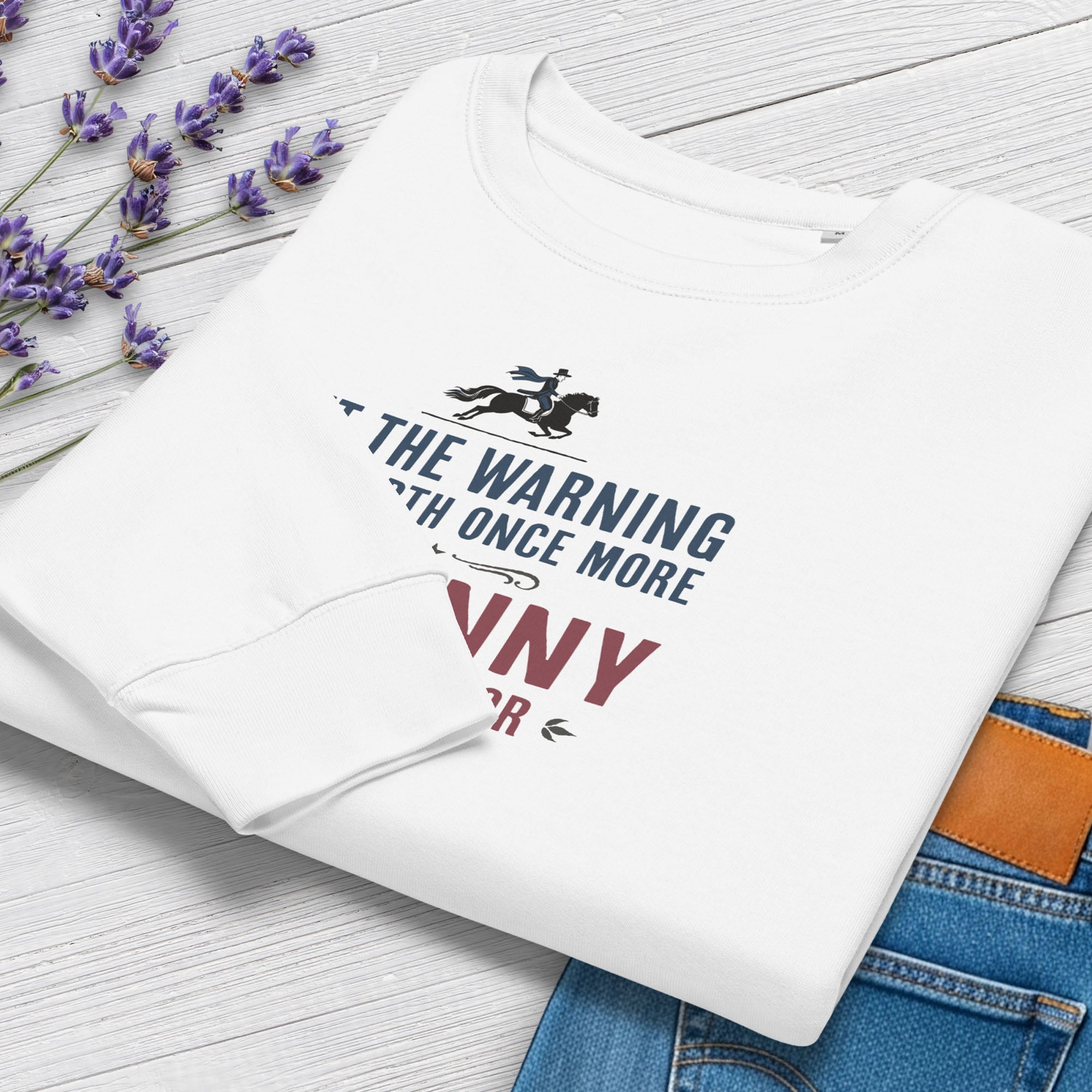 Folded white sweatshirt with a silhouette of Paul Revere on horseback and the text “Let the warning ride forth once more – Tyranny is at our door” in blue and red, showing cuff detail.
