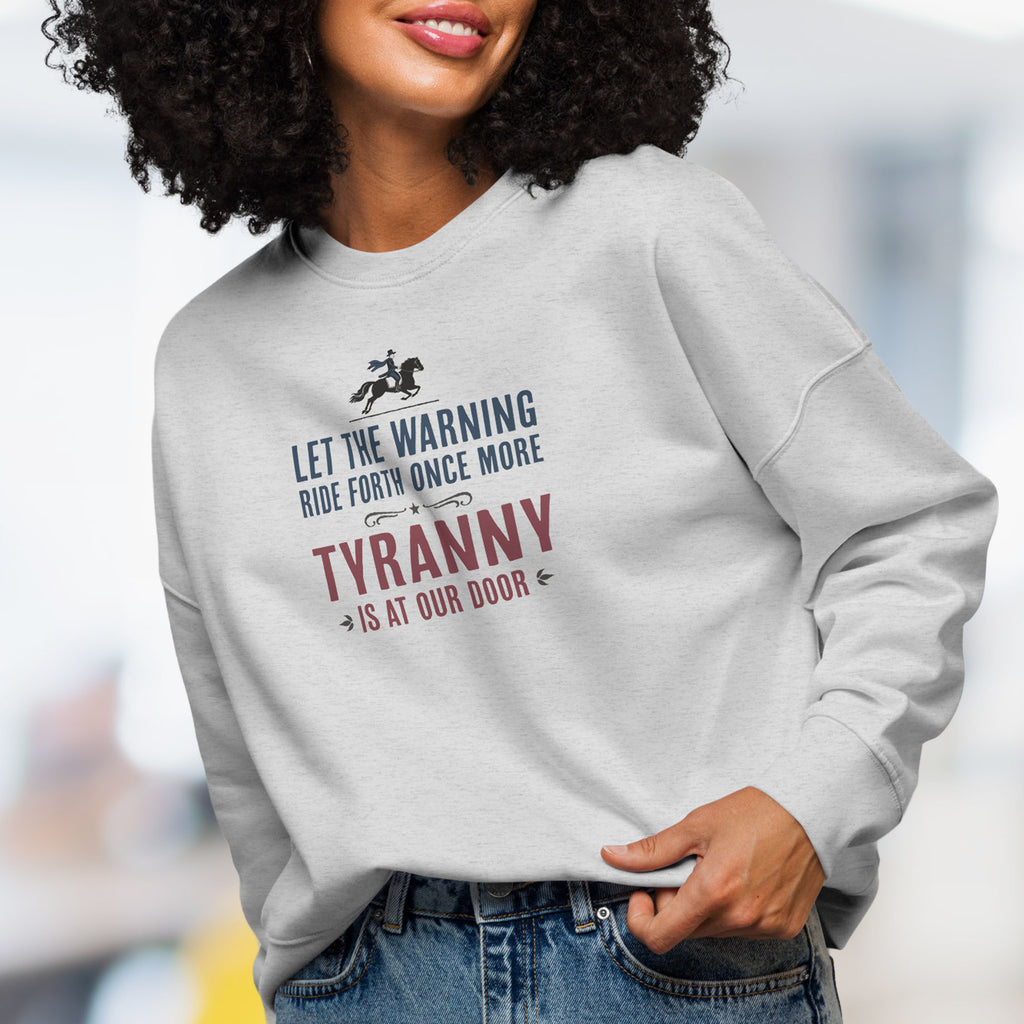 Front view of female model wearing grey sweatshirt with a silhouette of Paul Revere on horseback and the text “Let the warning ride forth once more – Tyranny is at our door” in blue and red.