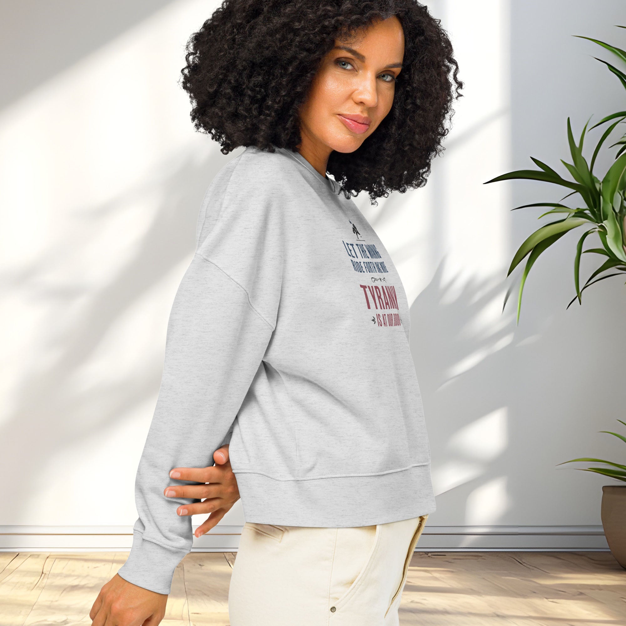 Side view of female model wearing grey sweatshirt with a silhouette of Paul Revere on horseback and the text “Let the warning ride forth once more – Tyranny is at our door” in blue and red.