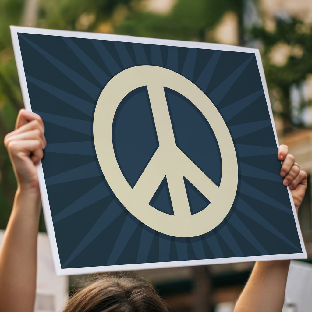 Person holding protest sign with golden peace symbol on a dark blue background with dark blue burst behind it.