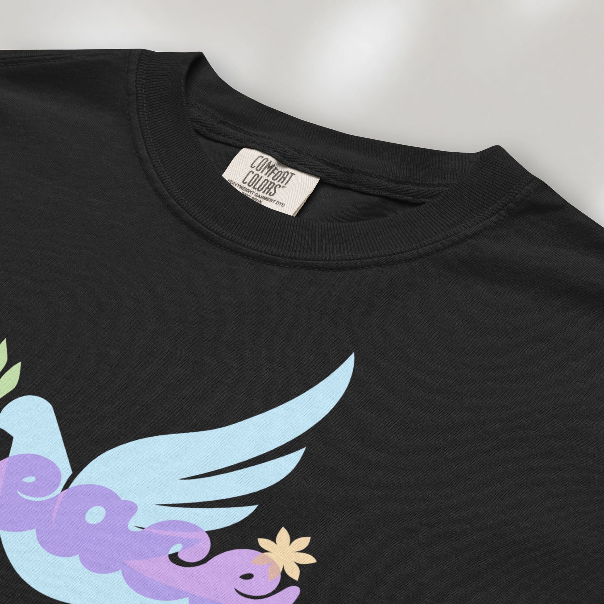 Closeup detail of black t-shirt featuring a colorful retro peace dove carrying an olive branch with the word "peace" in groovy 1970s-style lettering. 