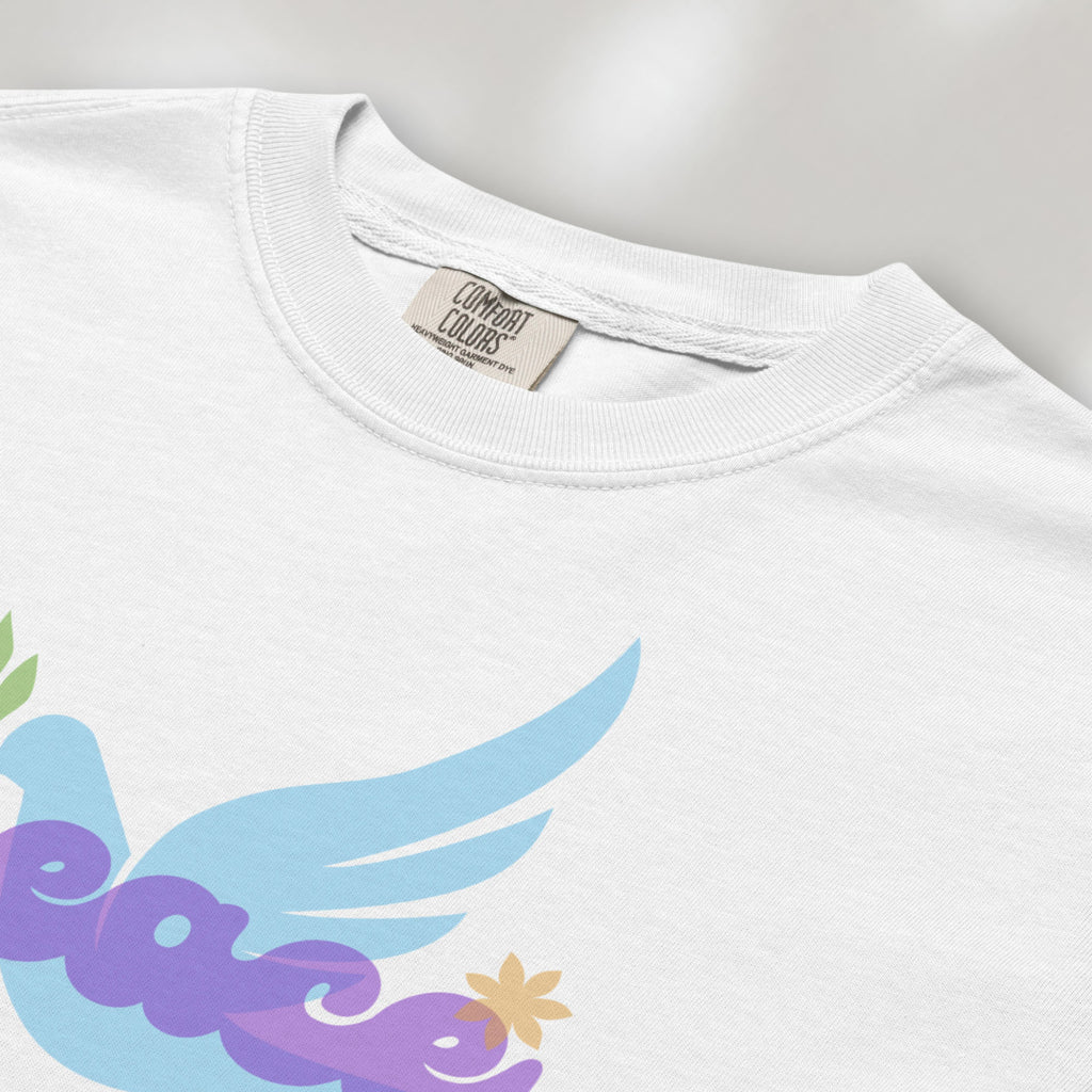 Closeup detail of white t-shirt featuring a colorful retro peace dove carrying an olive branch with the word "peace" in groovy 1970s-style lettering. 