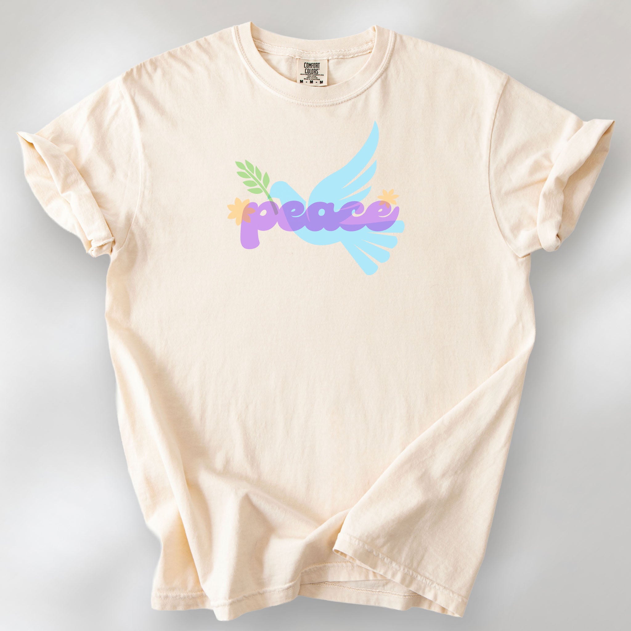 Ivory t-shirt featuring a colorful retro peace dove carrying an olive branch with the word "peace" in groovy 1970s-style lettering. 
