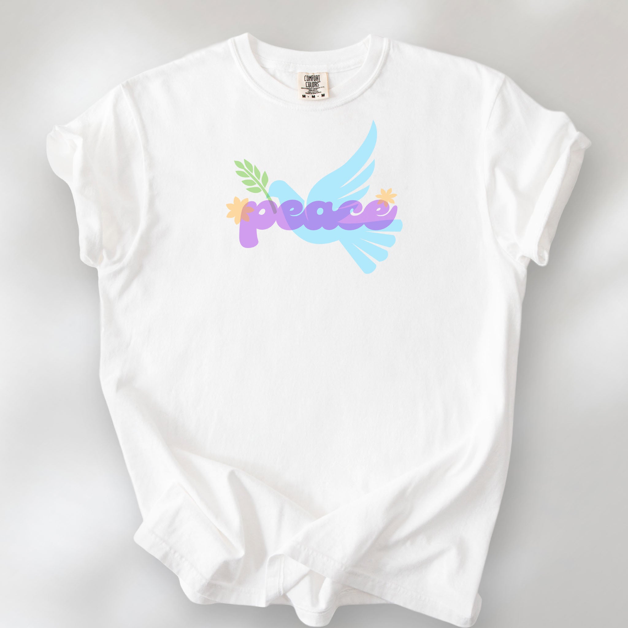 White t-shirt featuring a colorful retro peace dove carrying an olive branch with the word "peace" in groovy 1970s-style lettering. 