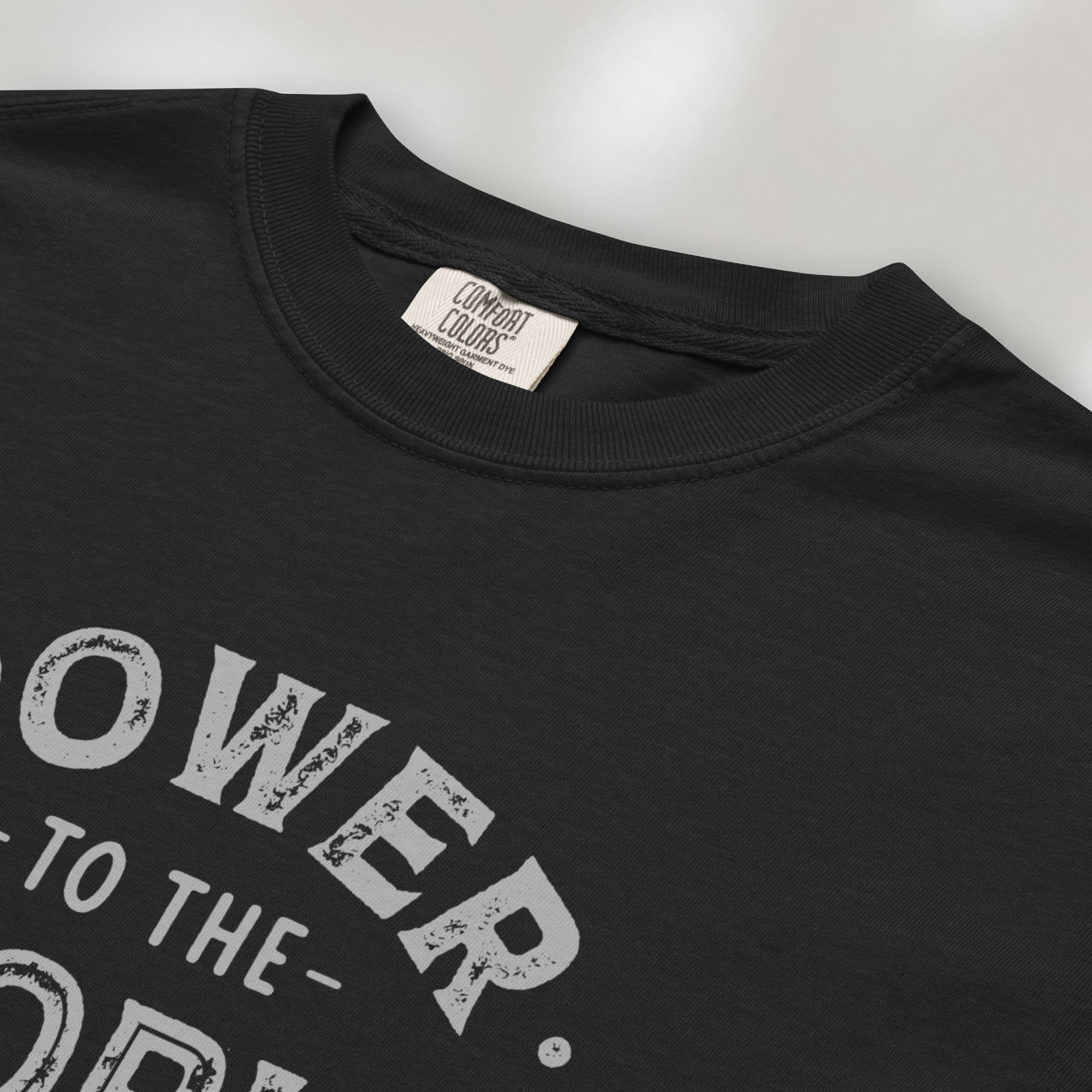 Closeup detail of black t-shirt with vintage-style distressed text reading “Power to the People — Show Up Speak Out”.