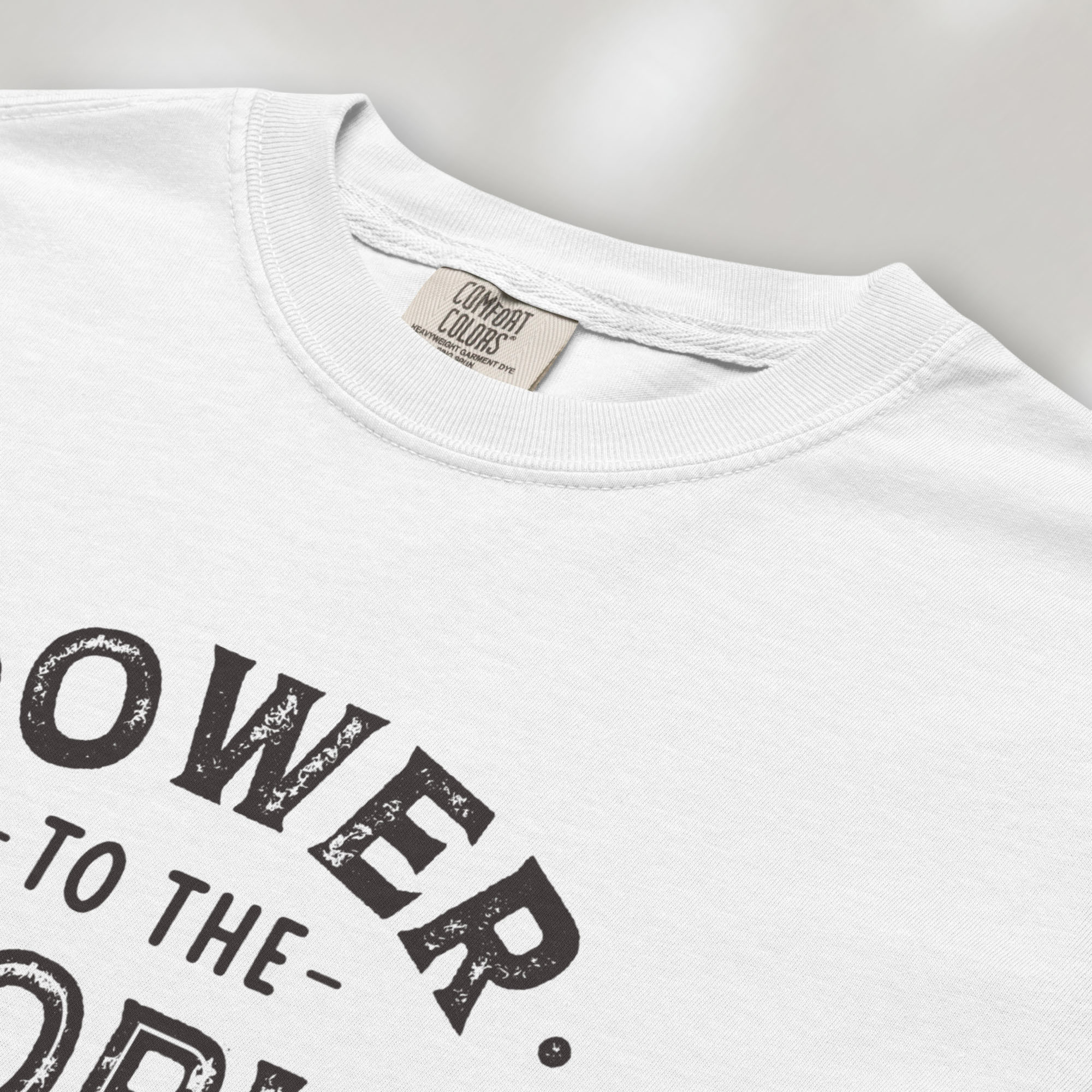 CLoseup detail of white t-shirt with vintage-style distressed text reading “Power to the People — Show Up Speak Out”.