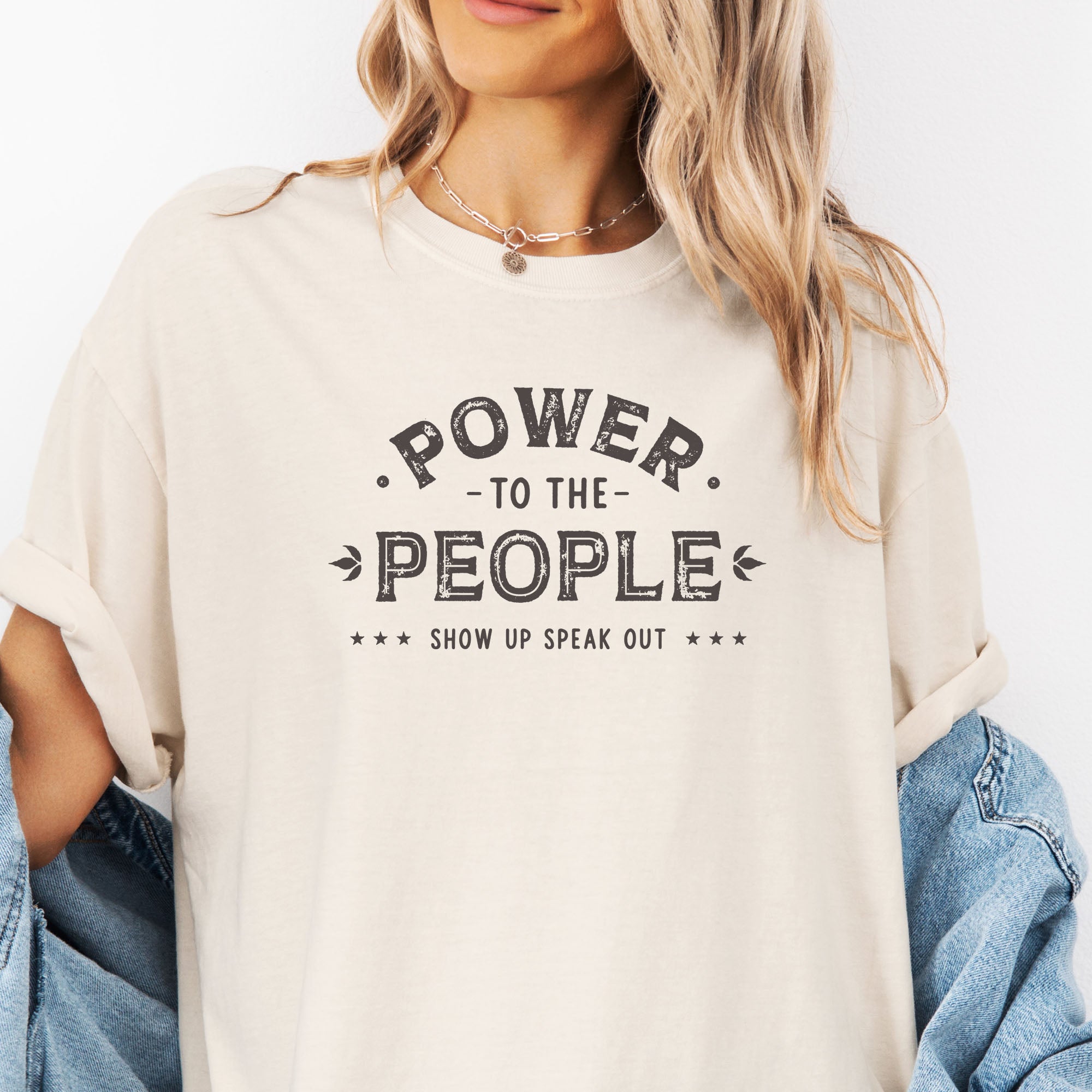 Female model wearing oversized ivory t-shirt with vintage-style distressed text reading “Power to the People — Show Up Speak Out”.