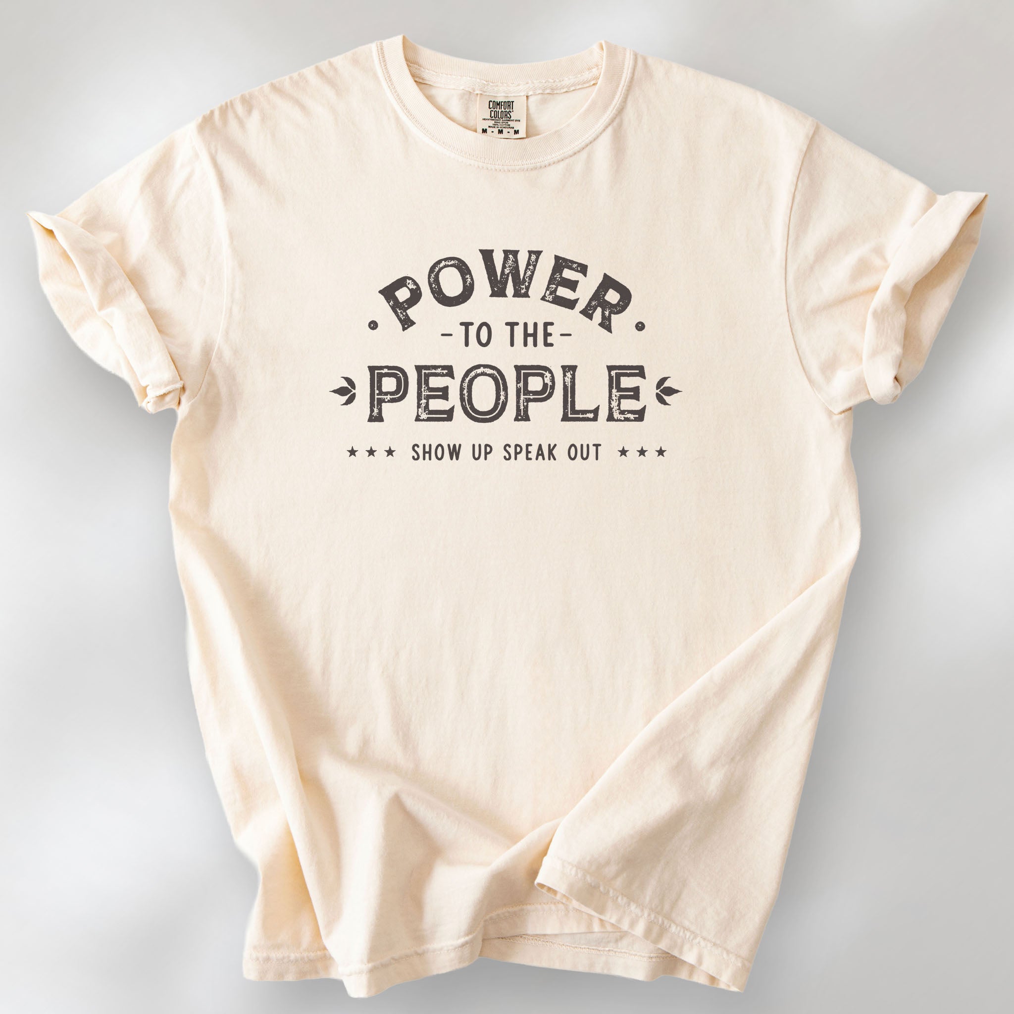 Ivory t-shirt with vintage-style distressed text reading “Power to the People — Show Up Speak Out”.