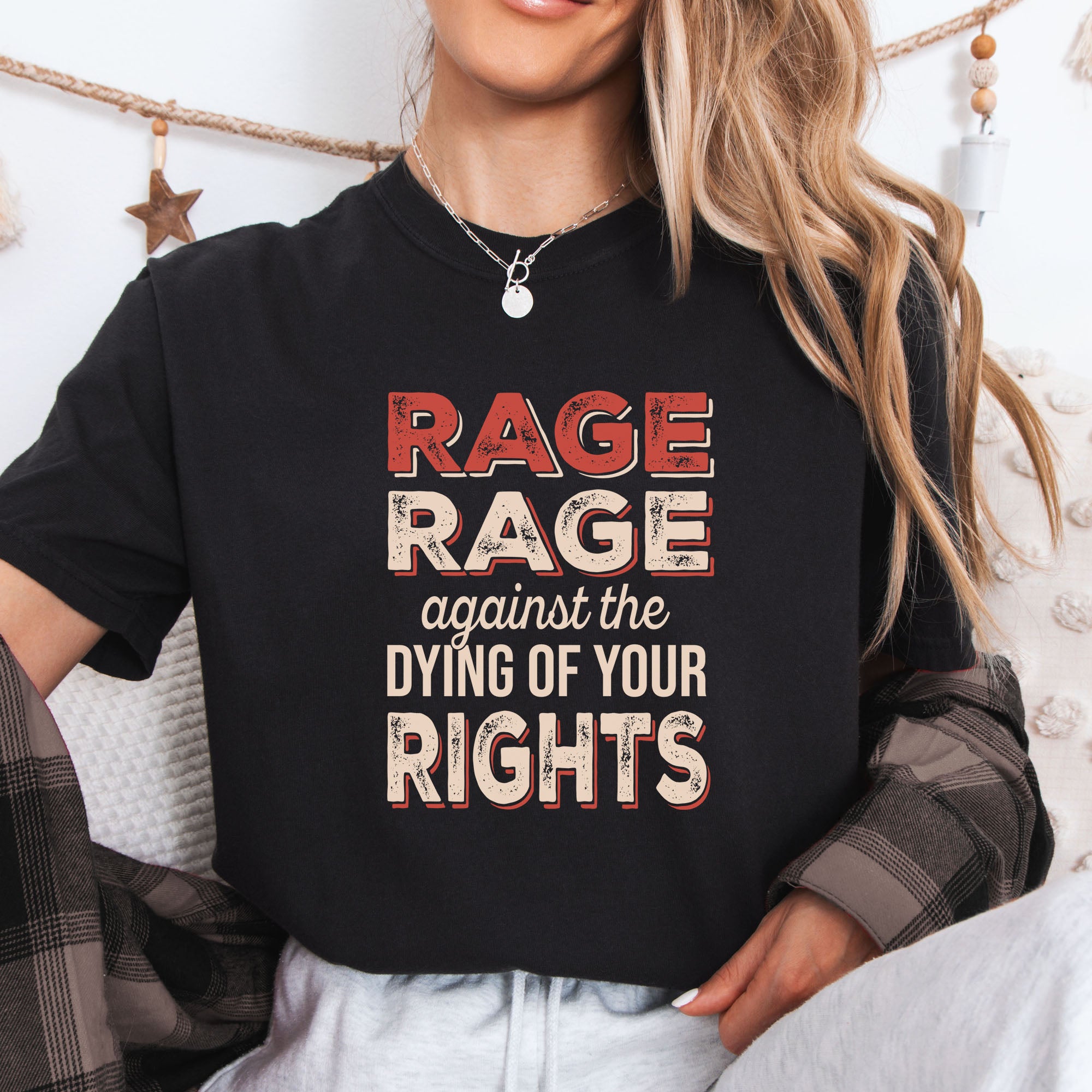 Female model wearing black unisex Comfort Colors 1717 t-shirt with bold distressed text that reads “RAGE RAGE against the DYING OF YOUR RIGHTS” in red and cream—political protest shirt for liberals and activists.