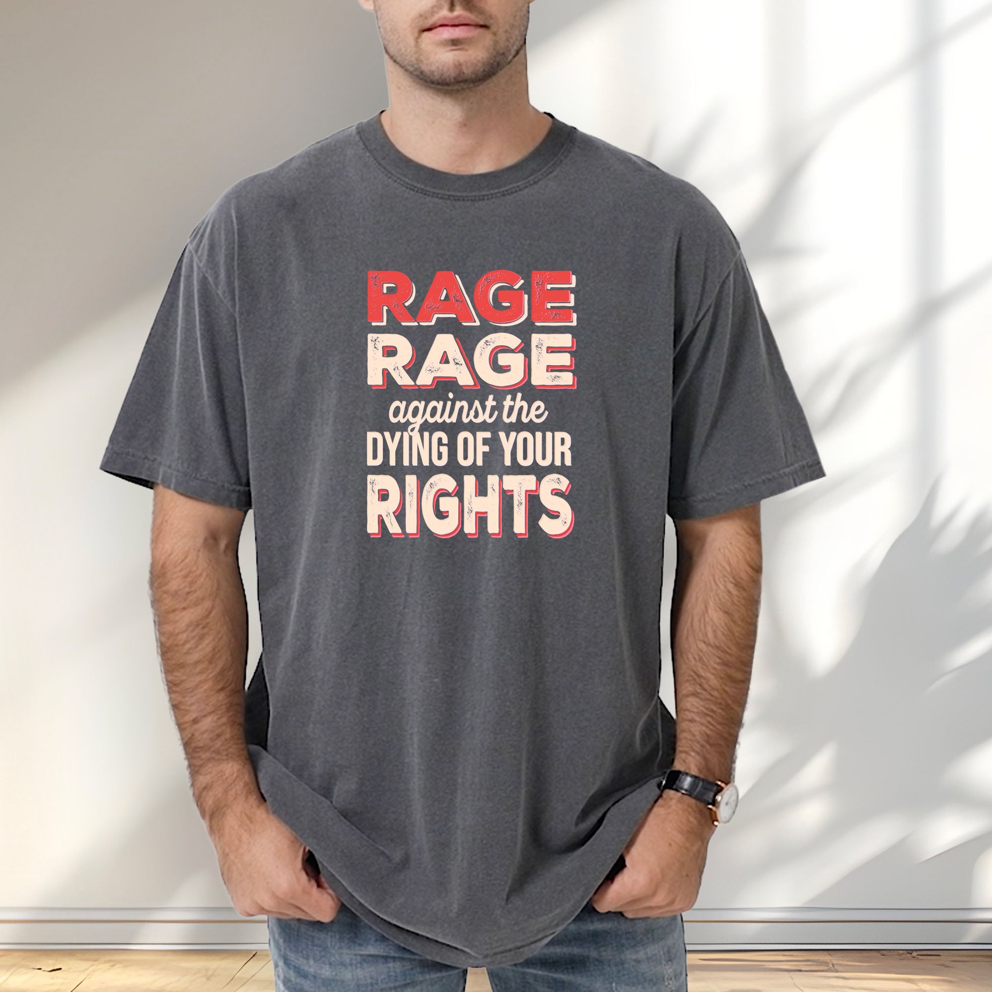 Male model wearing pepper unisex Comfort Colors 1717 t-shirt with bold distressed text that reads “RAGE RAGE against the DYING OF YOUR RIGHTS” in red and cream—political protest shirt for liberals and activists.