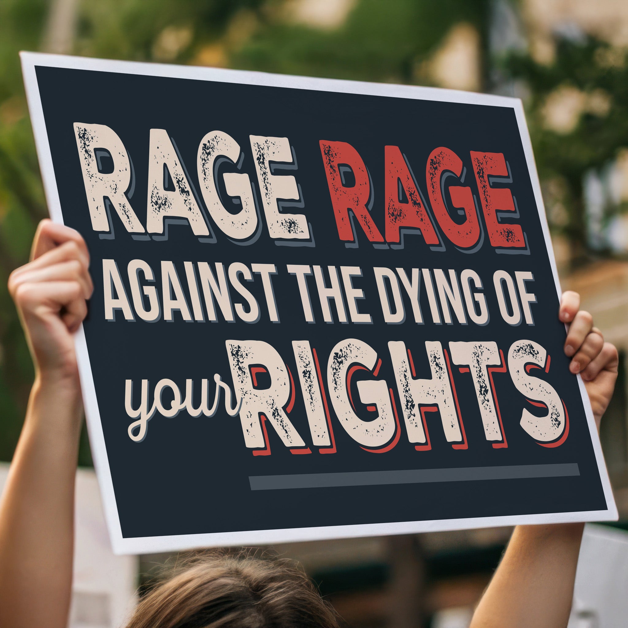 Protest sign with text that reads "Rage rage against the dying of your rights," a political twist to the line from a Dylan Thomas poem, held high in a crowd.
