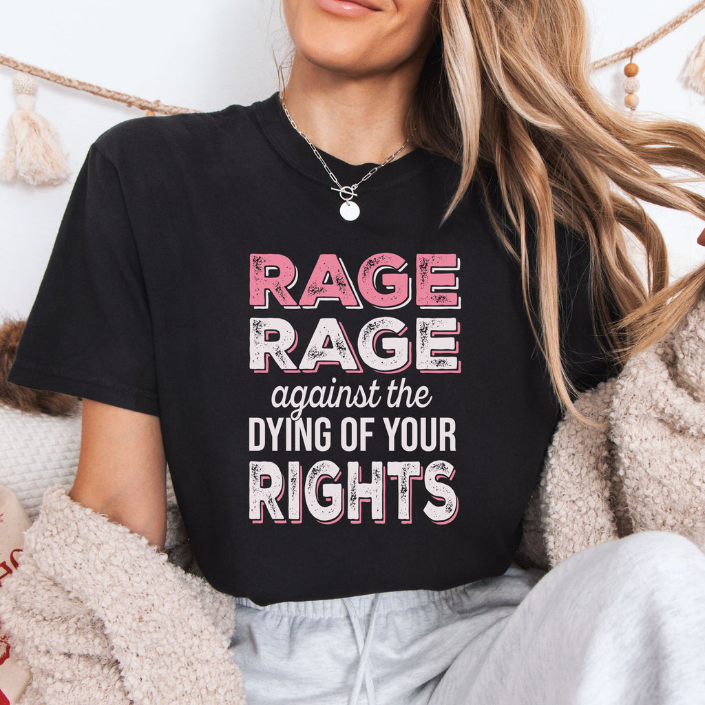 Female model wearing black protest t-shirt with bold pink and white text reading “rage rage against the dying of your rights” – feminist anti-trump activist shirt.