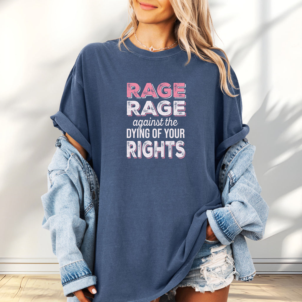 Female model wearing oversized denim protest t-shirt with bold pink and white text reading “rage rage against the dying of your rights” – feminist anti-trump activist shirt.