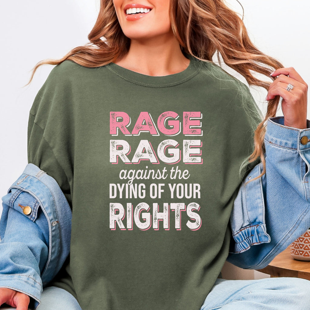 Female model wearing sage protest t-shirt with bold pink and white text reading “rage rage against the dying of your rights” – feminist anti-trump activist shirt.