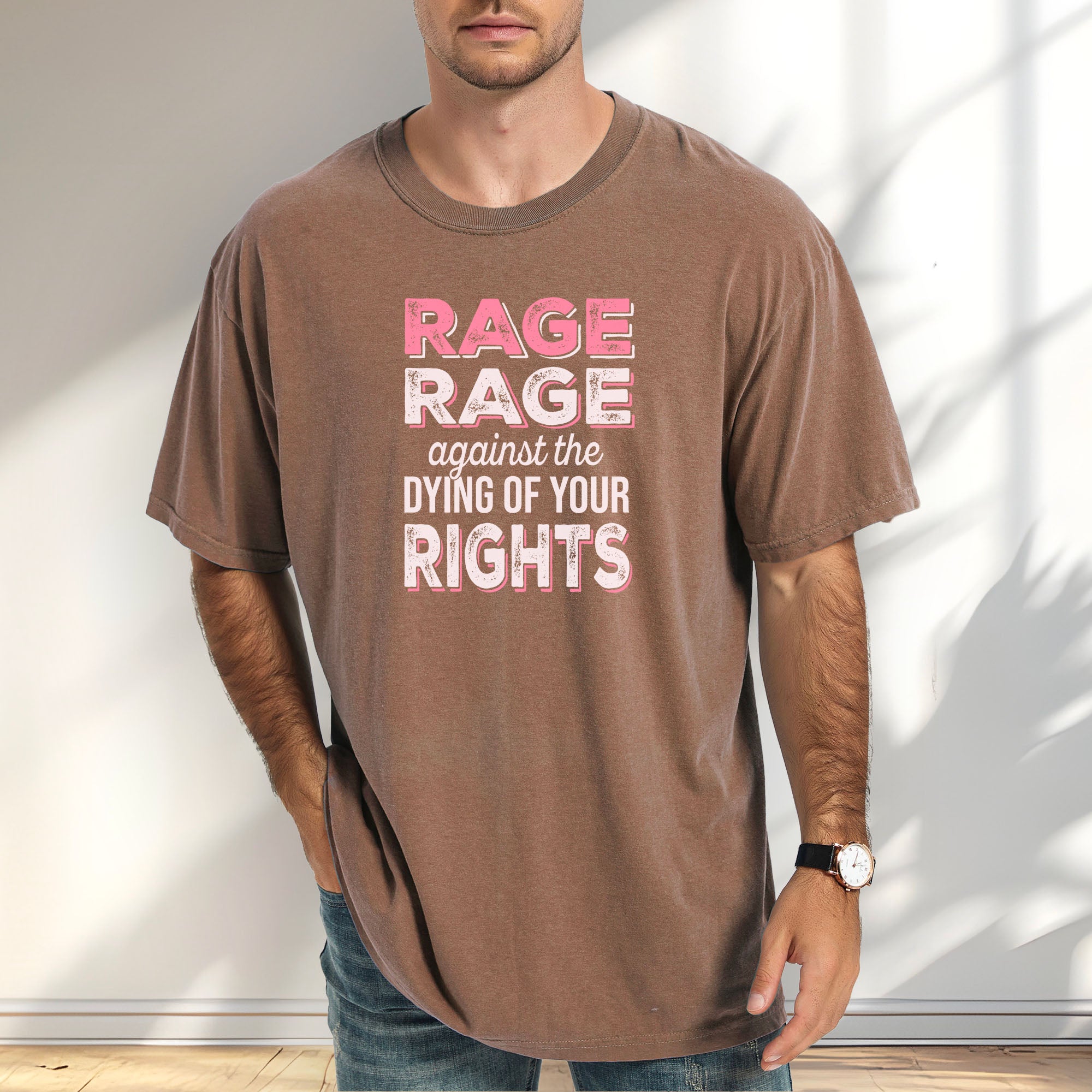 Male model wearing espresso protest t-shirt with bold pink and white text reading “rage rage against the dying of your rights” – feminist anti-trump activist shirt.