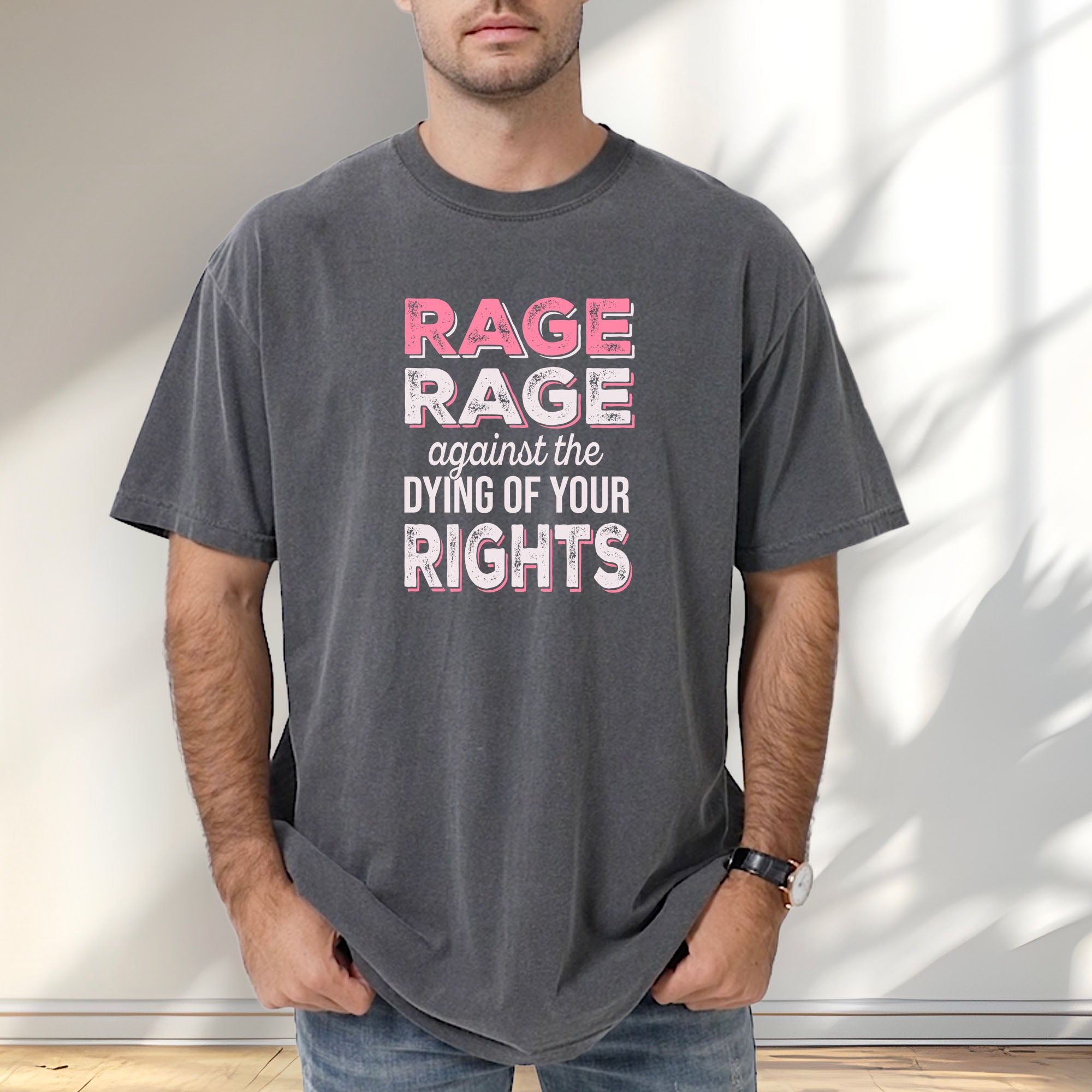 Male model wearing pepper protest t-shirt with bold pink and white text reading “rage rage against the dying of your rights” – feminist anti-trump activist shirt.