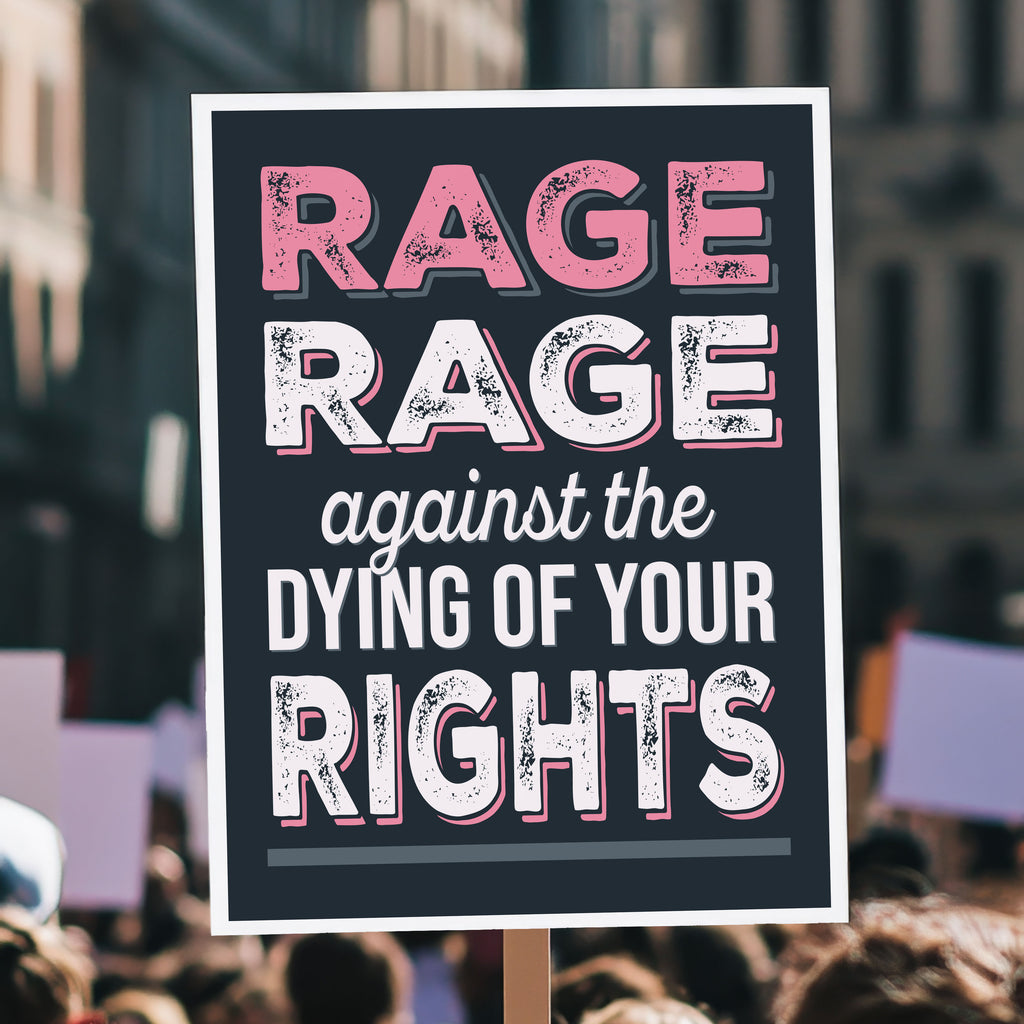 Protest sign with bold distressed text that reads "Rage rage against the dying of your rights," a political twist to the line from a Dylan Thomas poem, held high above a crowd.