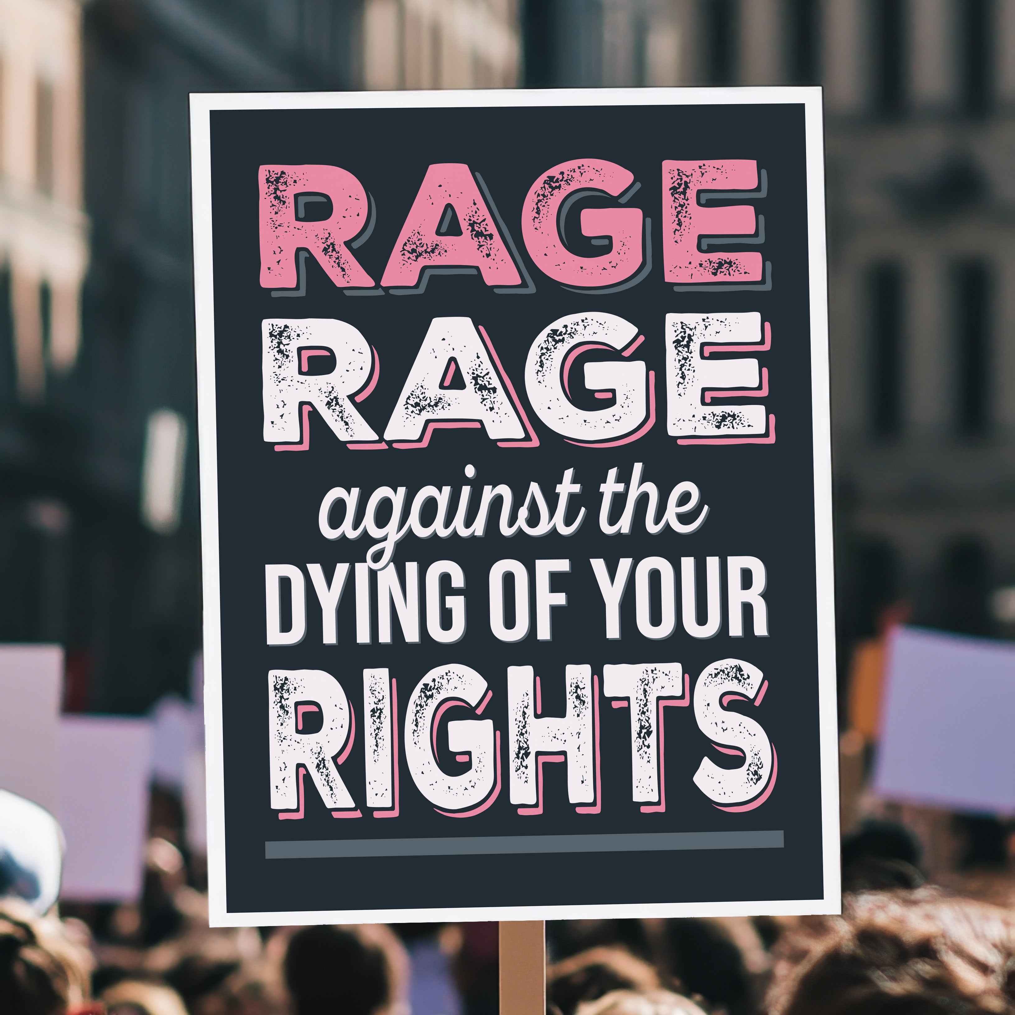 Protest sign with bold distressed text that reads "Rage rage against the dying of your rights," a political twist to the line from a Dylan Thomas poem, held high above a crowd.
