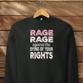 Black protest sweatshirt with bold pink and white text reading “rage rage against the dying of your rights” – feminist anti-trump activist shirt.