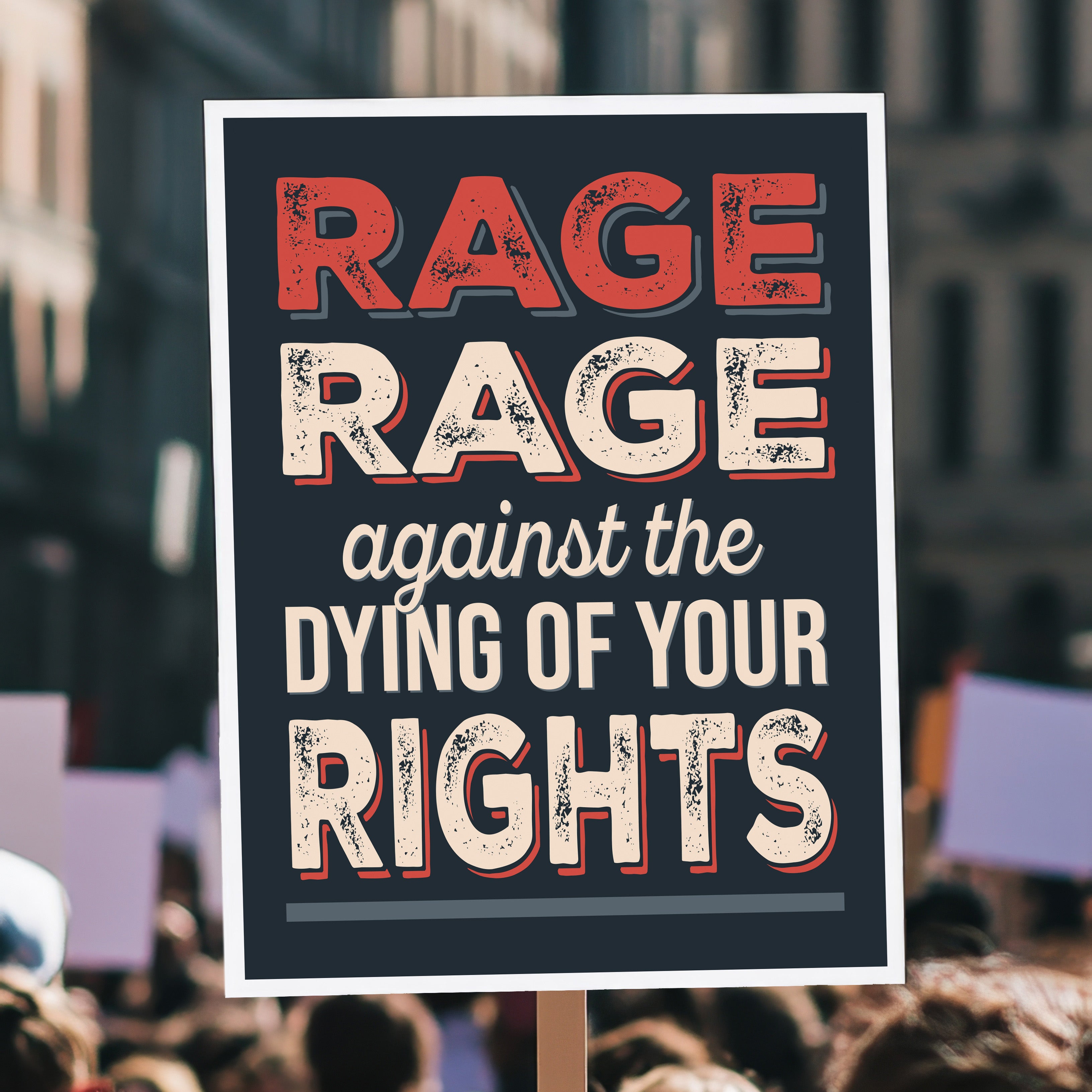 Protest sign with bold distressed text that reads "Rage rage against the dying of your rights," a political twist to the line from a Dylan Thomas poem, held high above a crowd.
