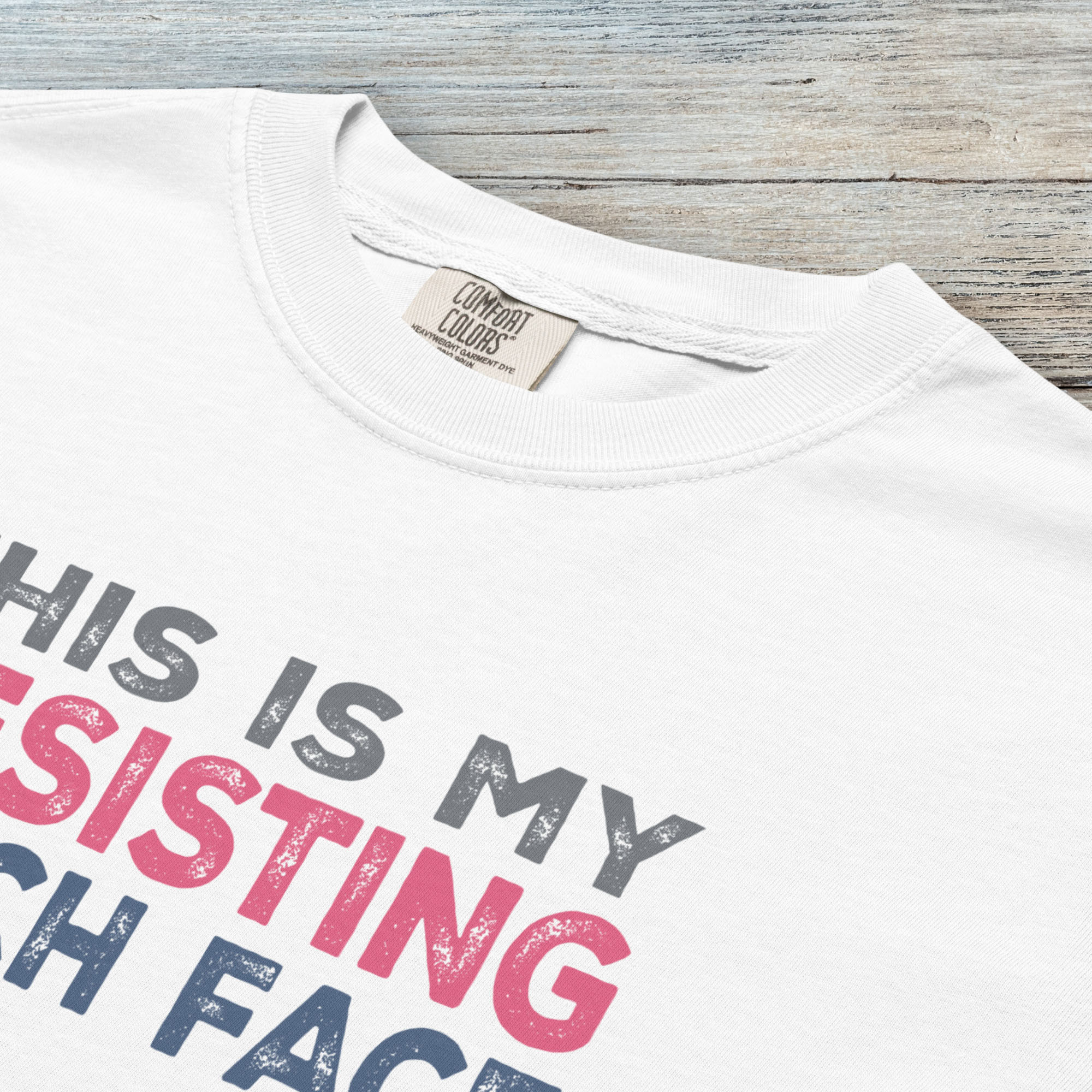 Closeup detail of white t-shirt with bold text that reads "This Is My Resisting Bitch Face" in gray, pink, and blue distressed font – a strong feminist and political protest shirt ideal for activism and making a bold statement.