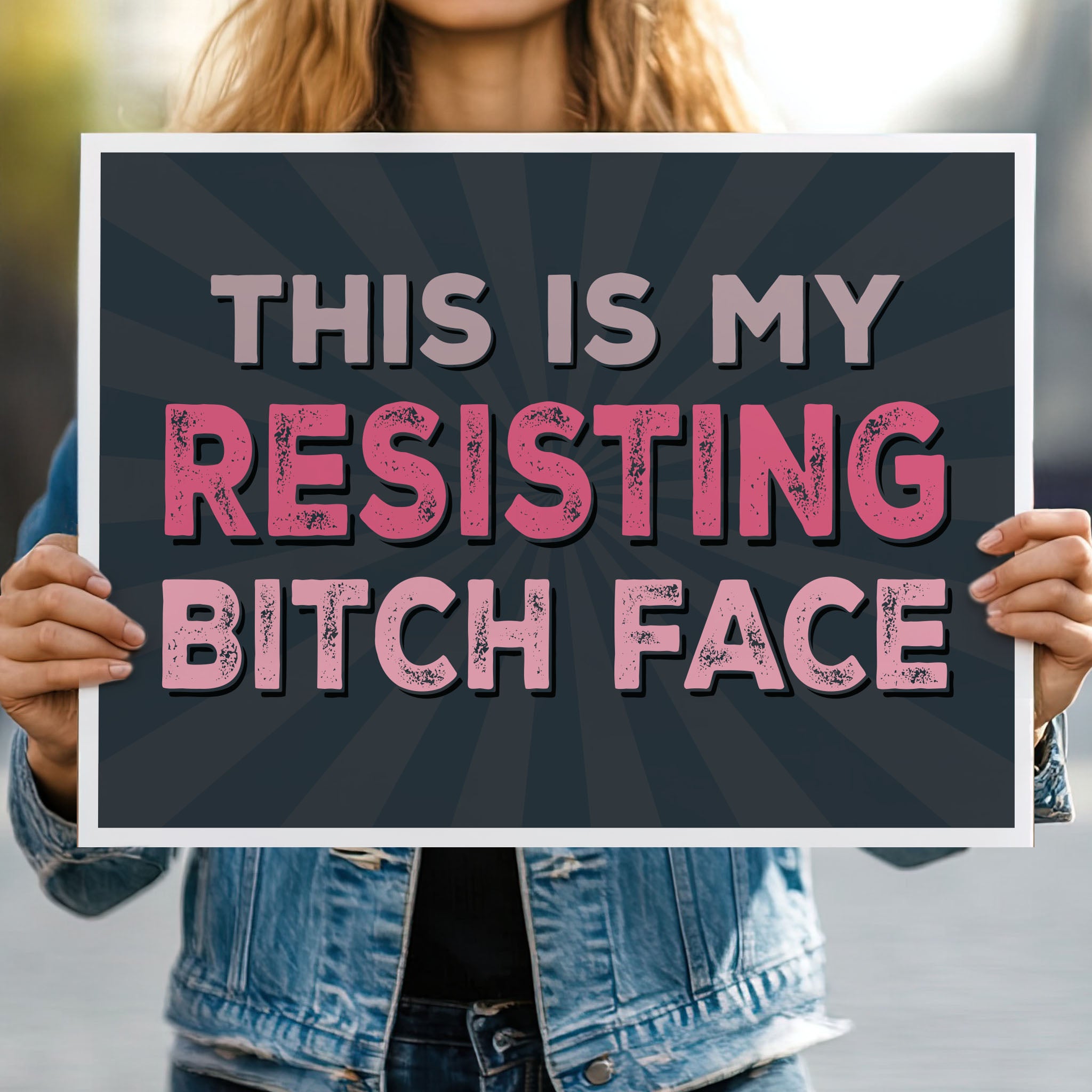 Person holding protest sign with a black background and pink distressed text that reads "This is my resisting bitch face" in all uppercase letters.